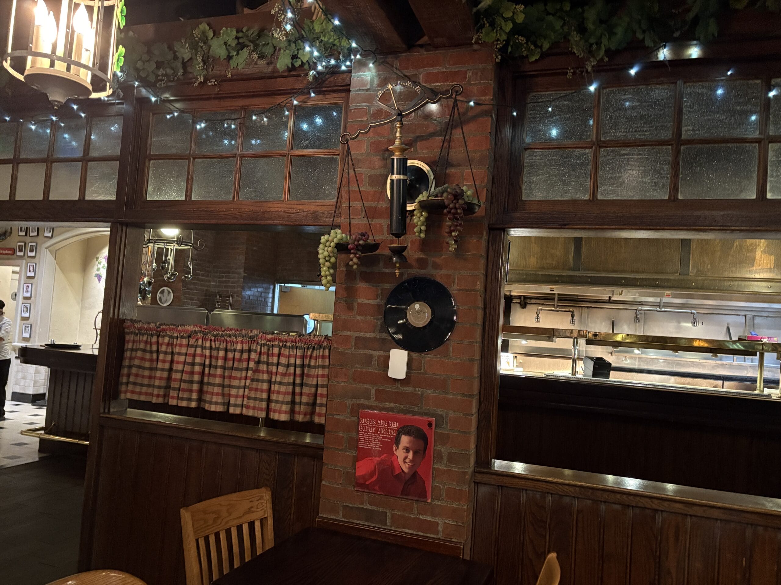 A cozy interior at Mama Melrose’s Ristorante Italiano with brick walls, string lights, grapes, and vintage photos.