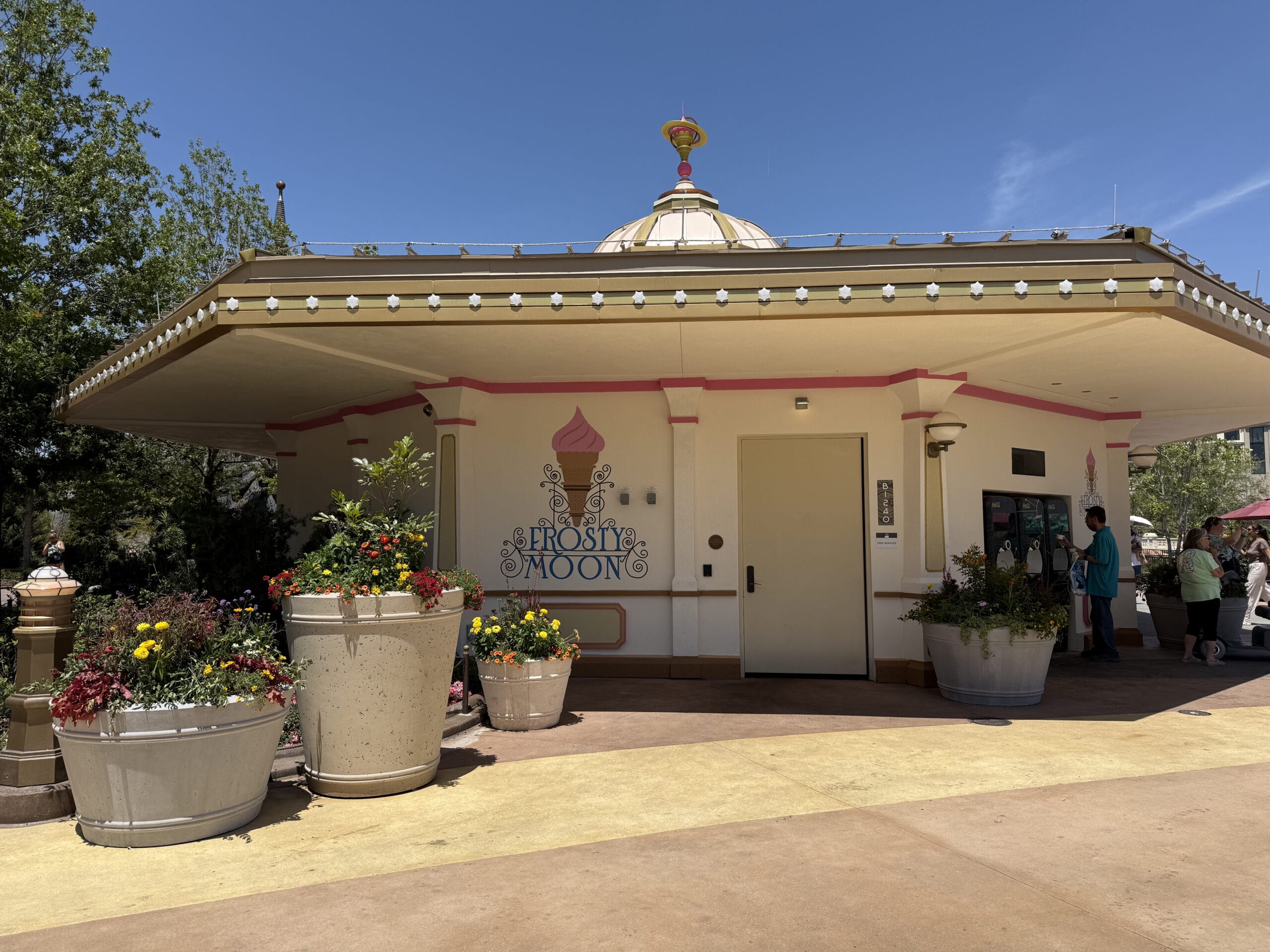 Small ice cream shop "Frost Moon" with large flower pots and people near the entrance enjoying Star Sui Bao on a sunny day.