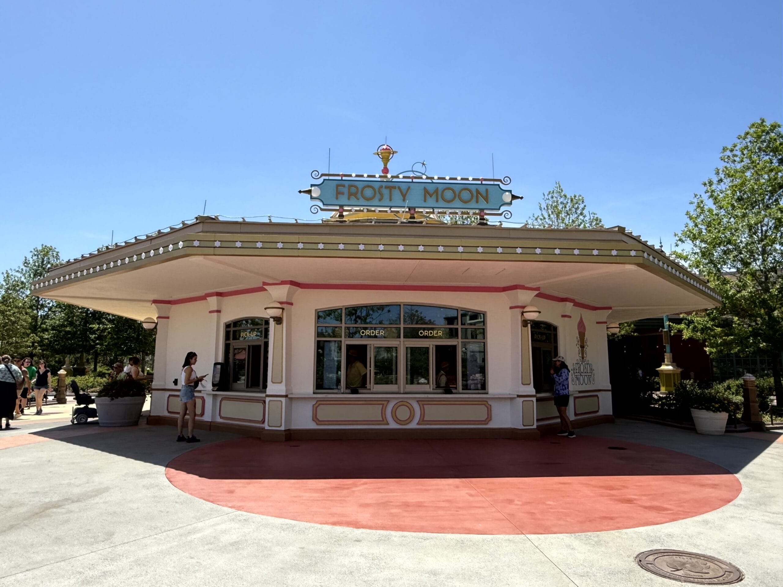 People gather by the retro-style Frosty Moon ice cream stand on a bright, sunny day.