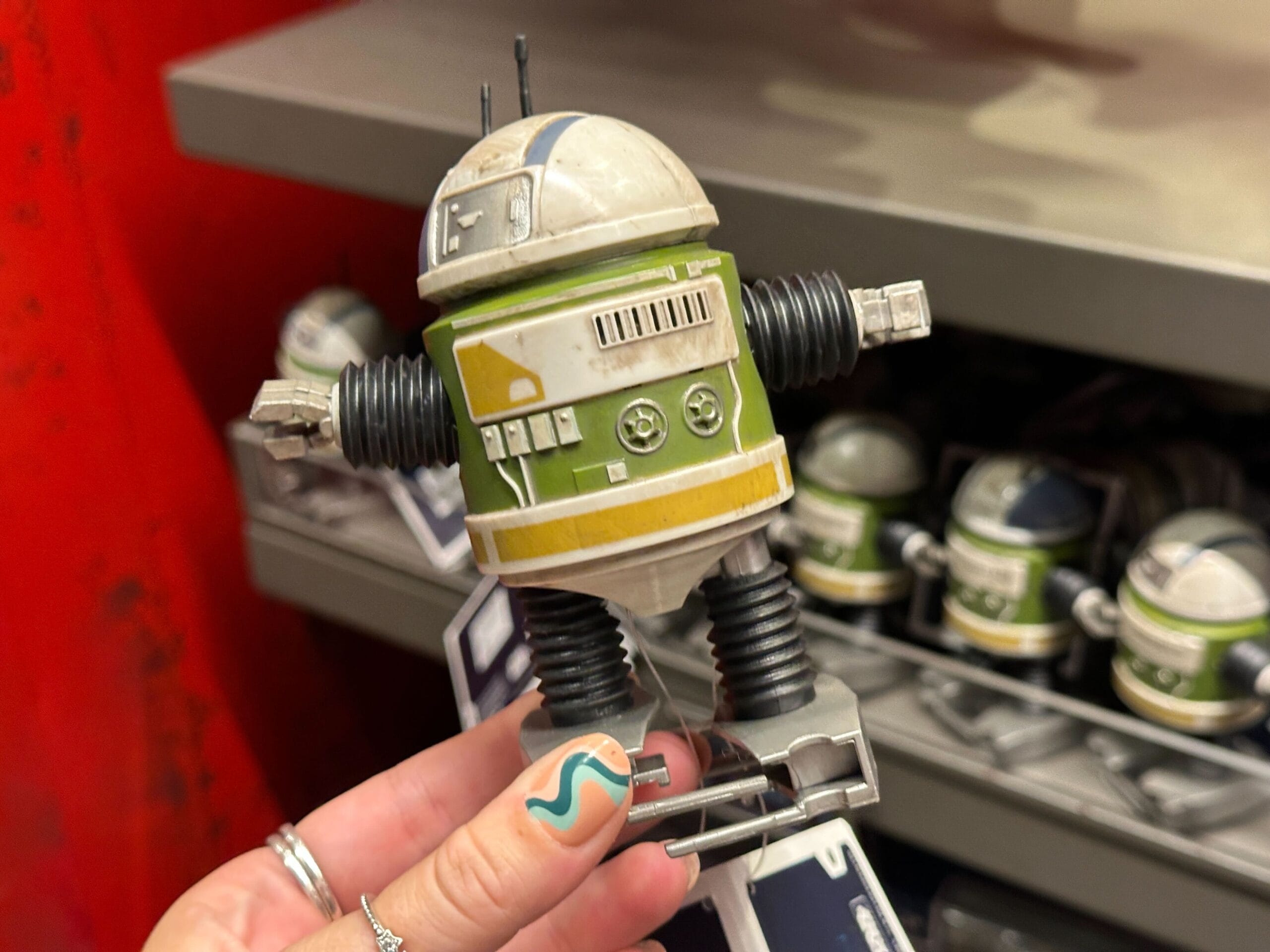 A hand holds a Clink Wind robot toy with spring legs and green details in a store display.