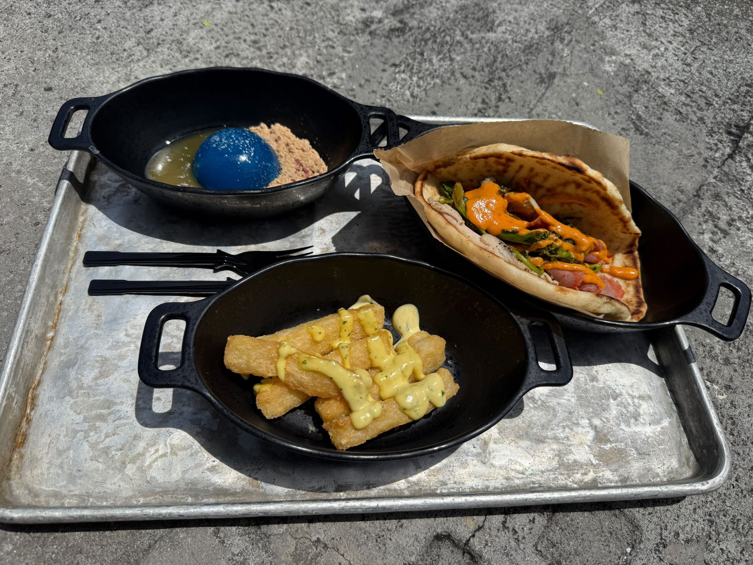 Three black dishes at Docking Bay 7: a blue dessert, fried sticks with sauce, and a veggie pita—perfect for Star Wars Day.