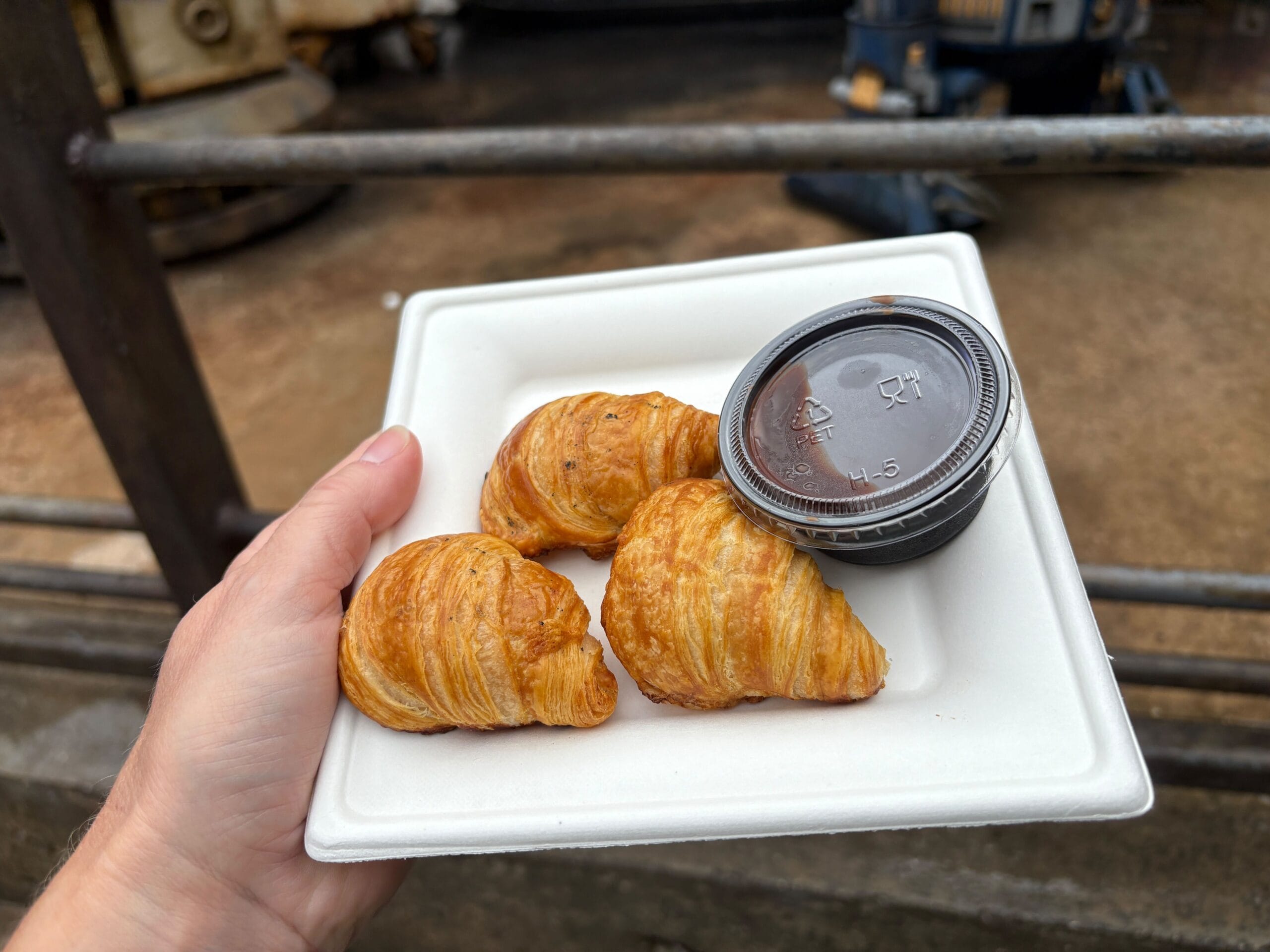 A hand holds a plate of Kessel Run Rations—three mini croissants and dipping sauce—at Disney's Hollywood Studios.