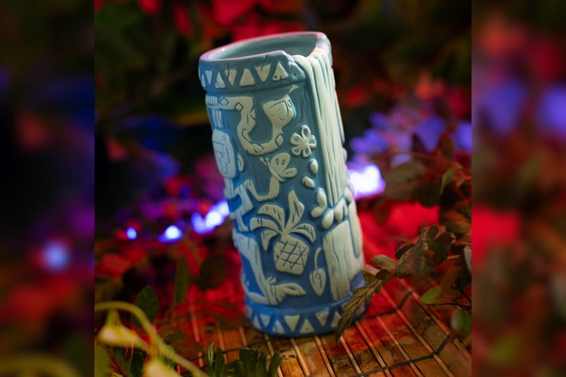 Blue ceramic Skipper's Adventure Tiki Mug with carved tropical designs, glowing lights, and foliage at Trader Sam's Grog Grotto.