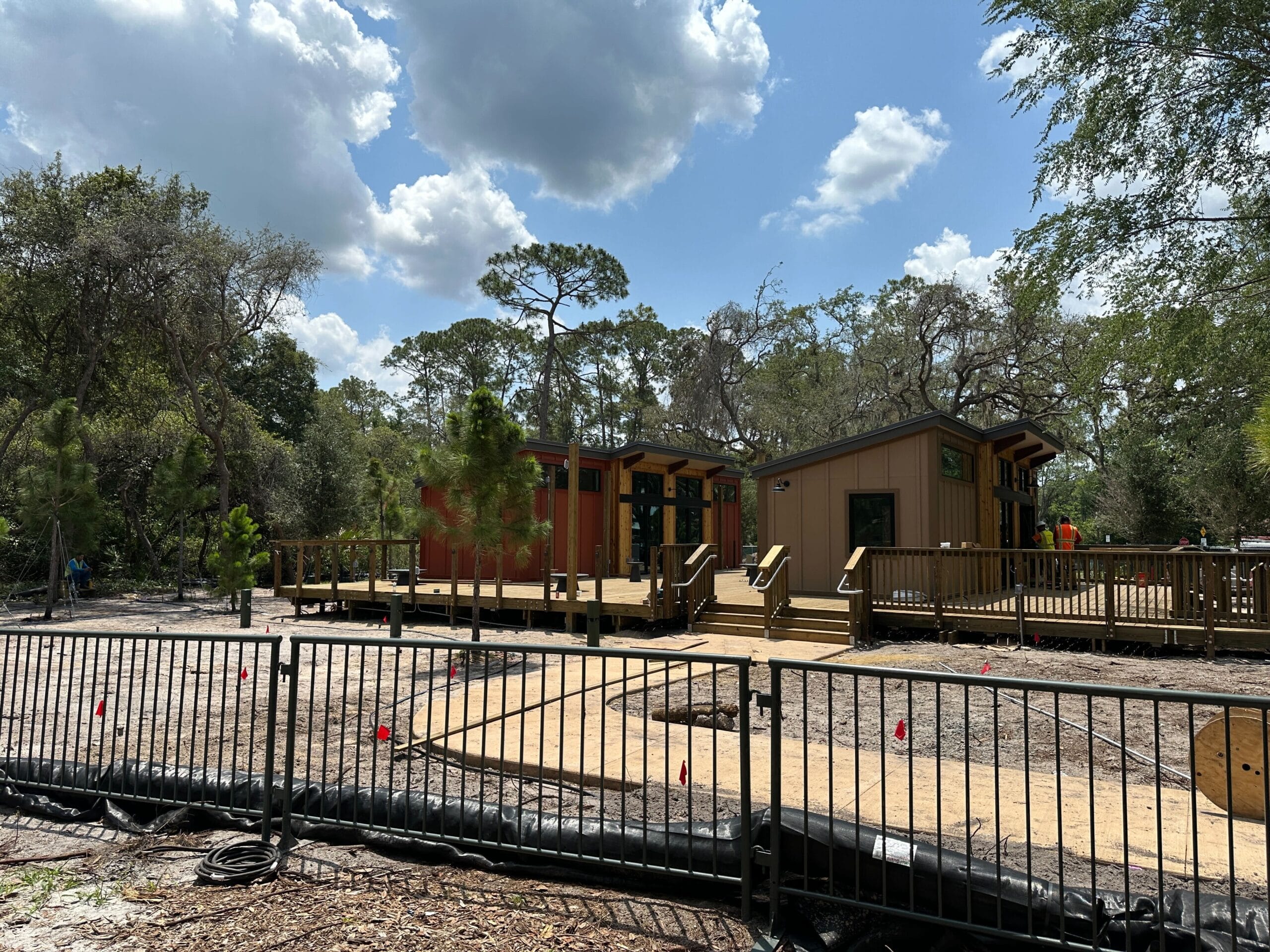 Single-story cabins with wooden decks, crafted by expert cabin contractors, nestled among trees behind a black fence.