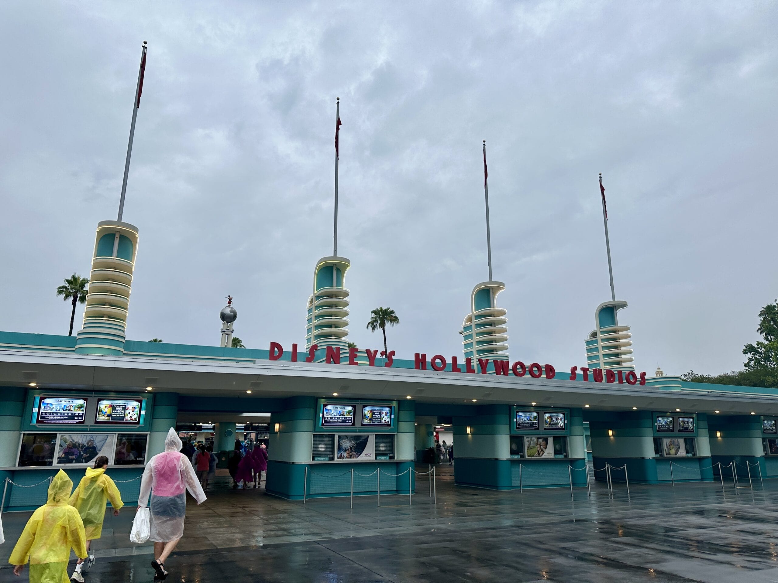 People in rain ponchos walk toward the entrance of Disney's MGM Studios on a cloudy, rainy day.
