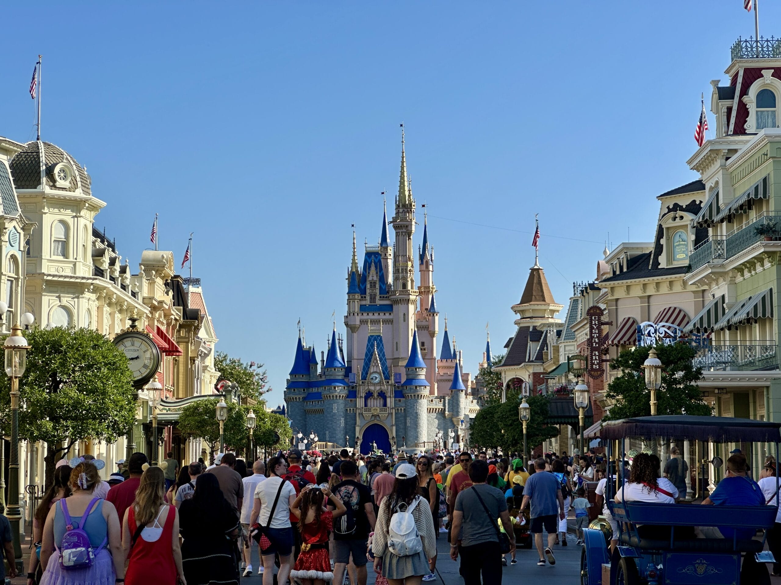A crowd walks toward Cinderella Castle at Magic Kingdom, enjoying a sunny day and browsing Disney park merchandise.