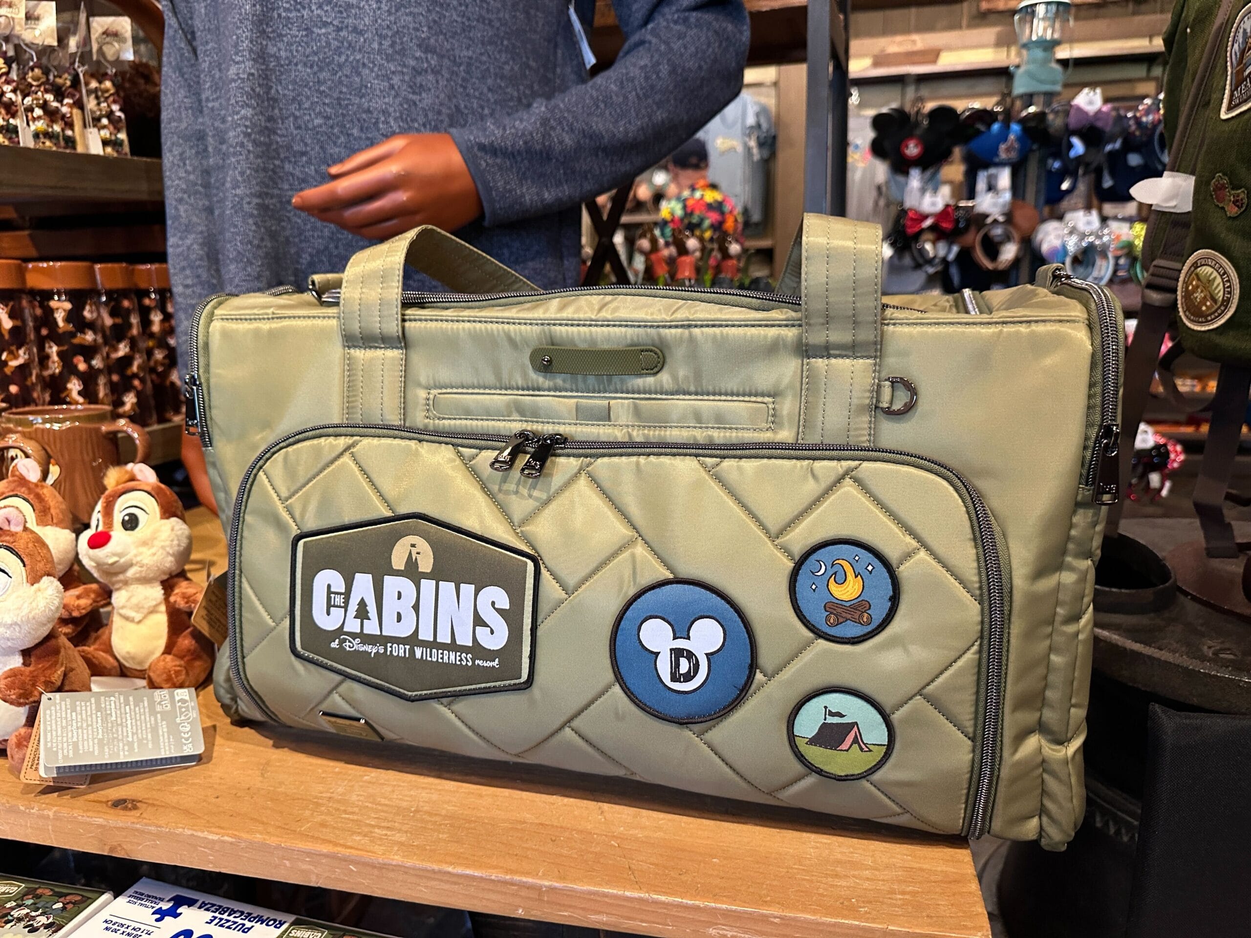 A green quilted Disney duffle bag with patches, inspired by Fort Wilderness Cabins, on a store shelf.