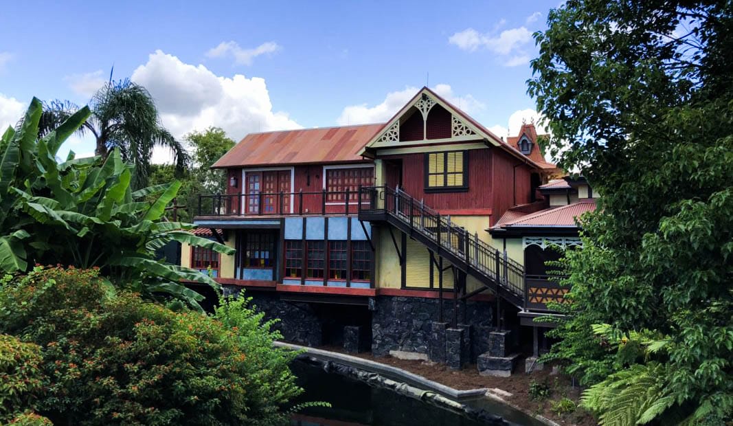 Club 33, a rustic, colorful wooden house in Adventureland is nestled among lush green trees under a partly cloudy sky.