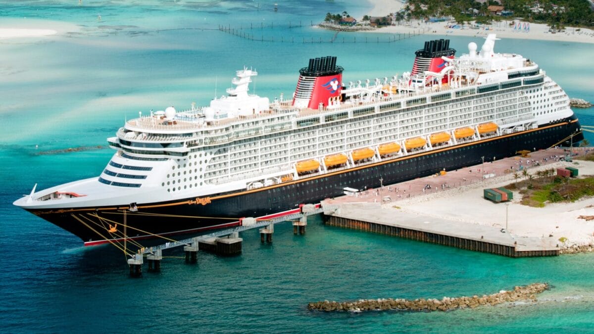 A Disney Cruise ship docked at the tropical port of Castaway Cay, surrounded by turquoise water and sandy beaches.