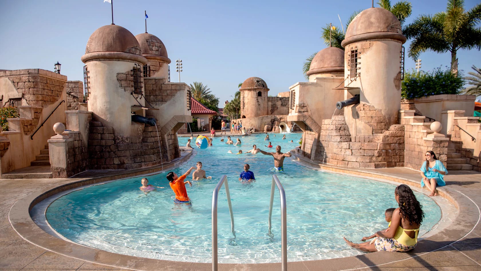 People swim and play in the Caribbean Beach resort pool with castle-like towers at Disney World Orlando.