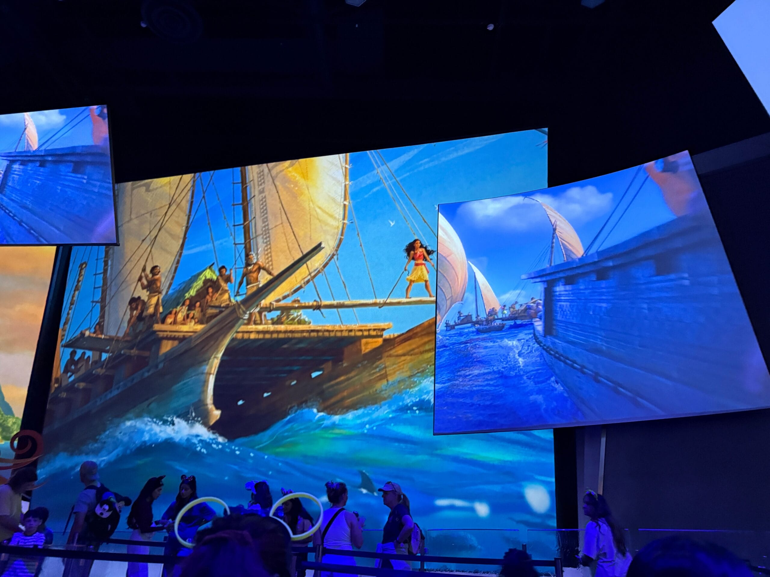 People view large screens displaying animated ocean scenes with boats and a girl standing on one of the boats.