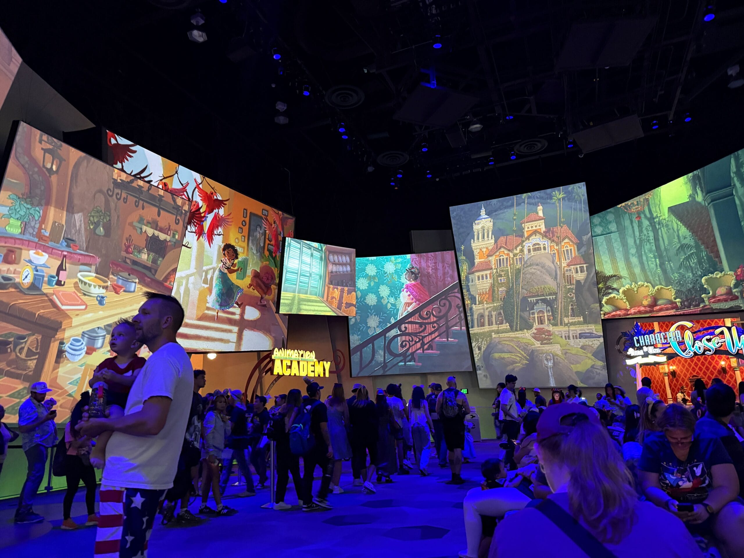 Crowd inside an indoor exhibit with colorful animated scenes from movies projected on large wall screens.