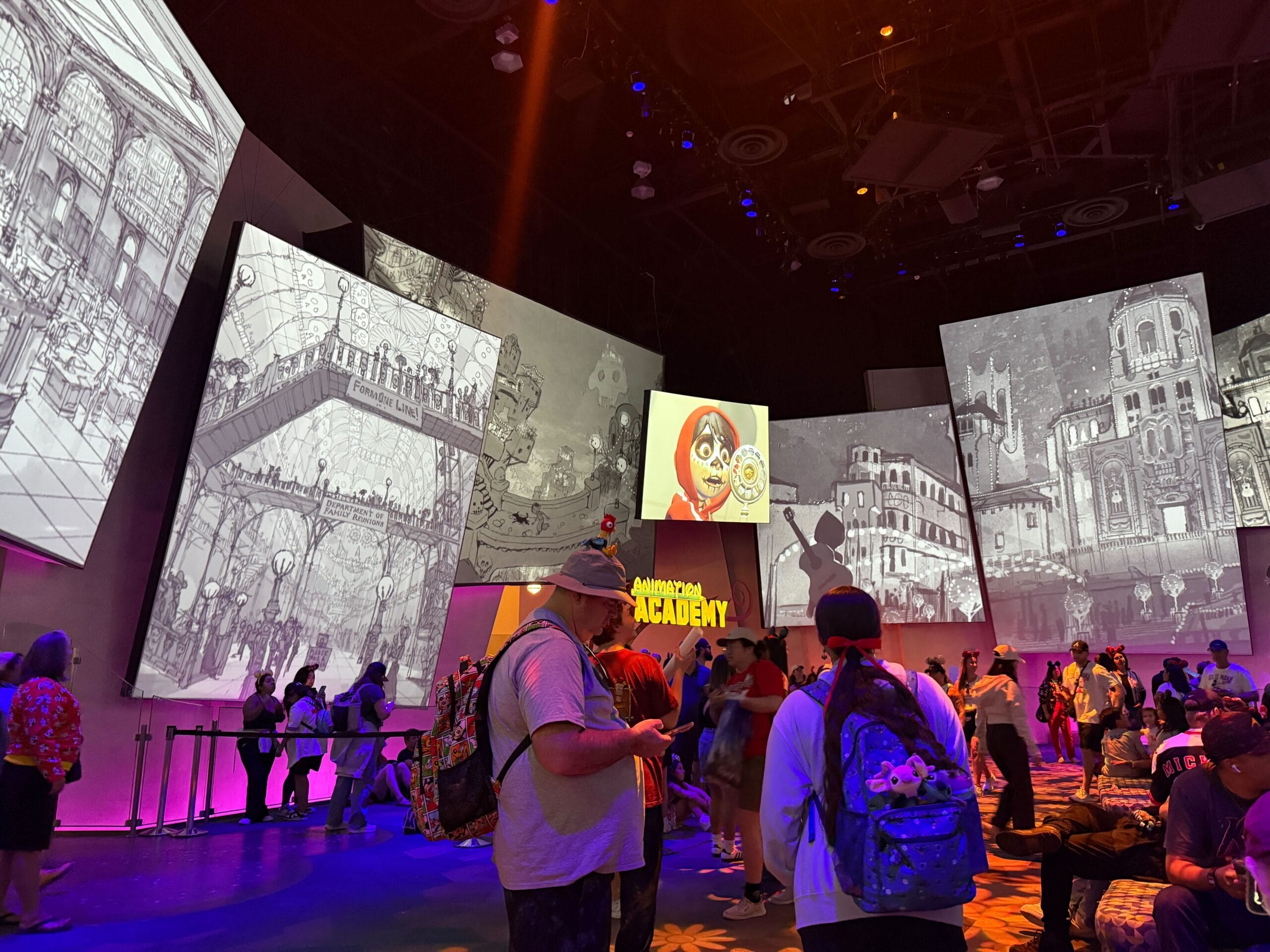 People stand inside an animation academy with sketches and character art projected on surrounding large screens.