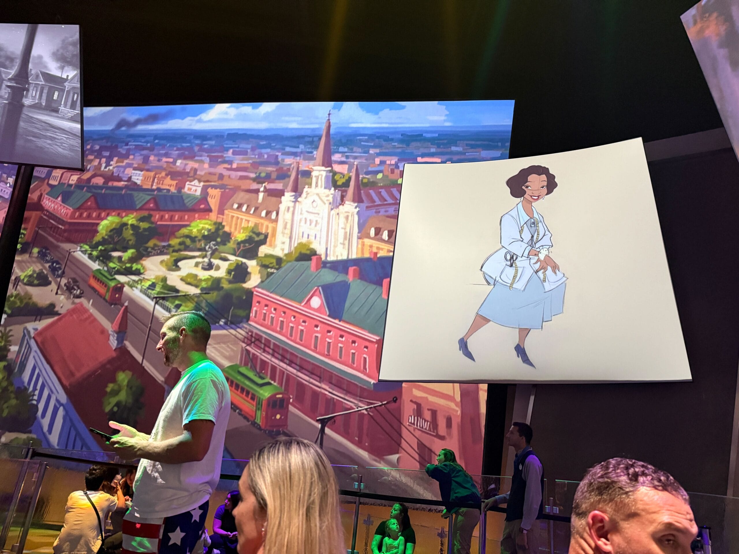 People stand indoors with cityscape art and a cartoon woman in a lab coat displayed on screens in the background.