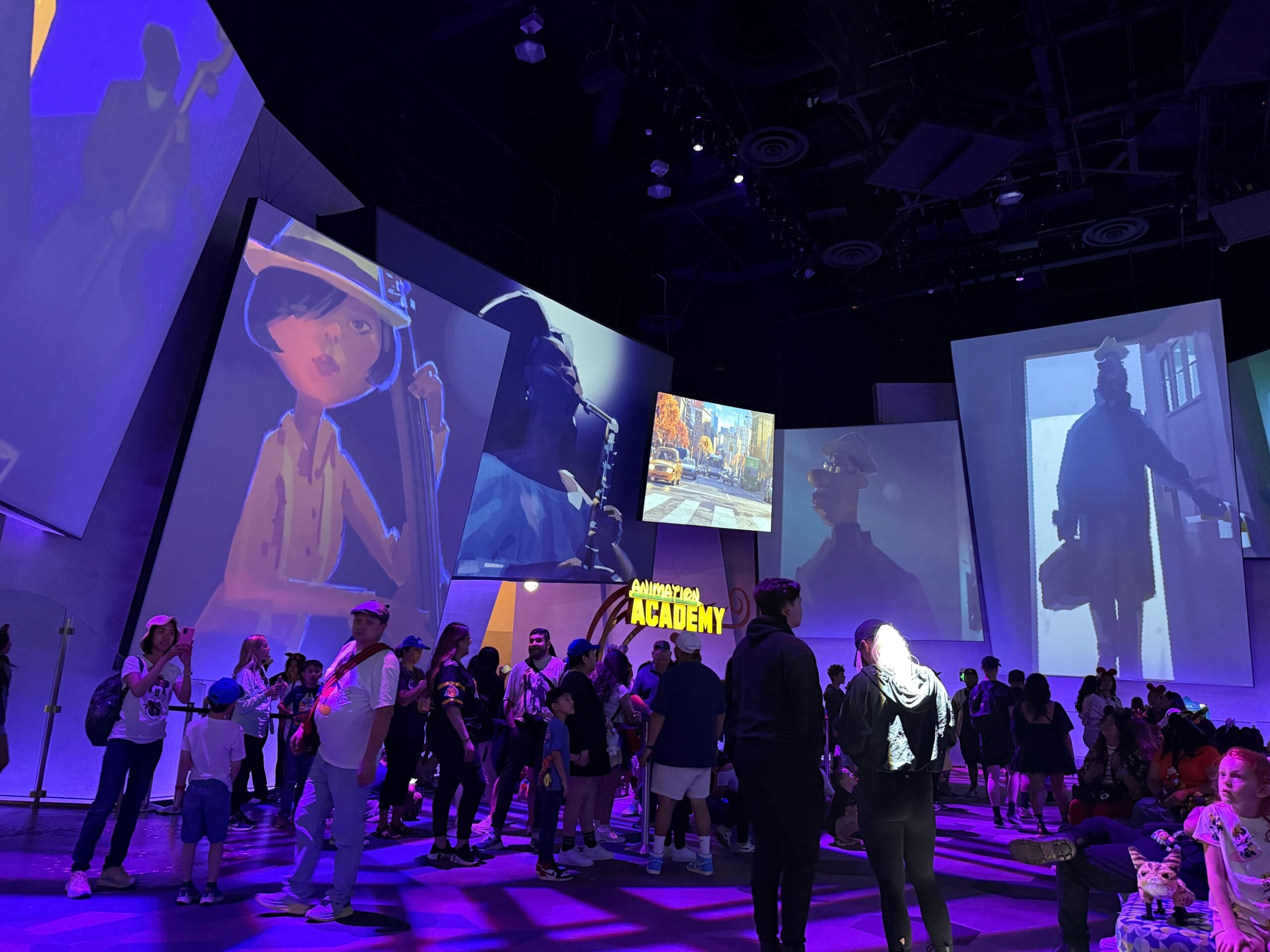 A crowd gathers inside a dimly lit room with large animated character projections on the walls.