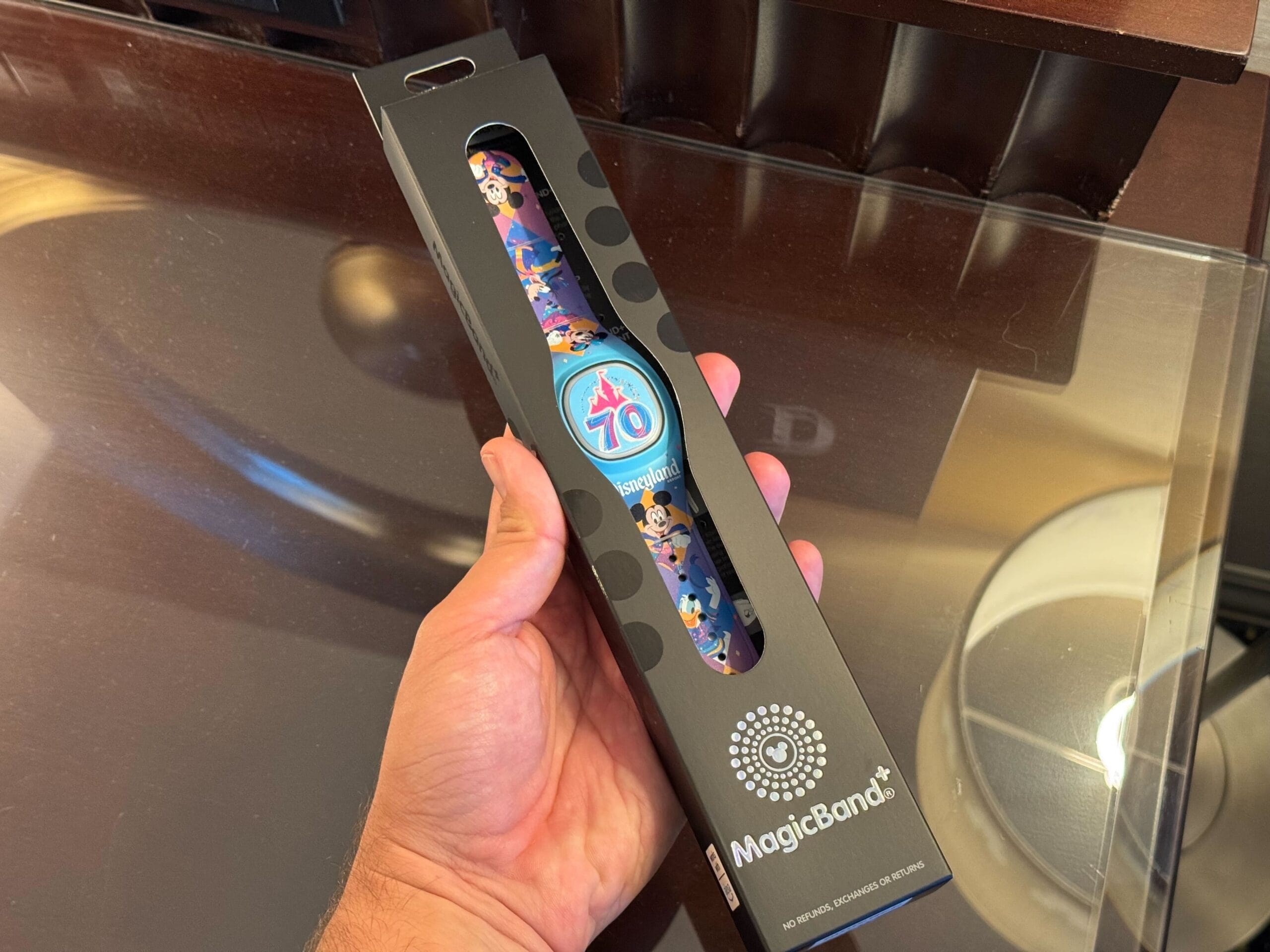 A hand holds a boxed MagicBand+ featuring a 70th Anniversary design with cartoon characters at Disneyland Resort.