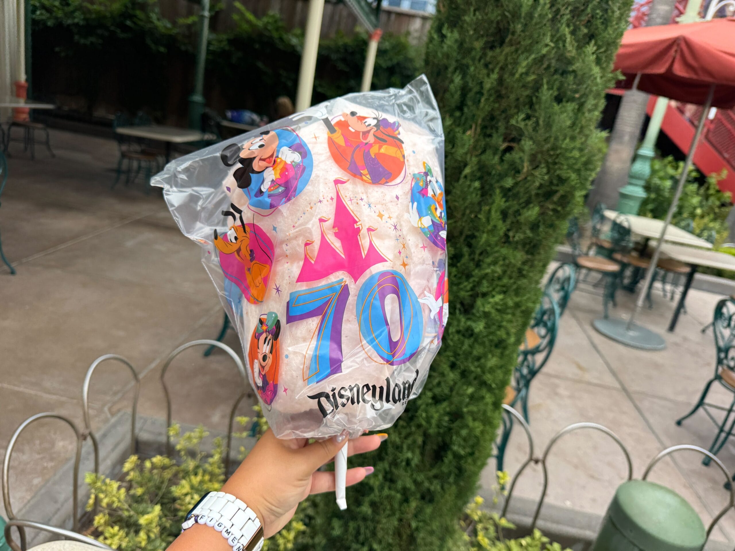 A hand holds Disneyland 70th anniversary cotton candy in themed packaging—perfect for any Disneyland food lover.
