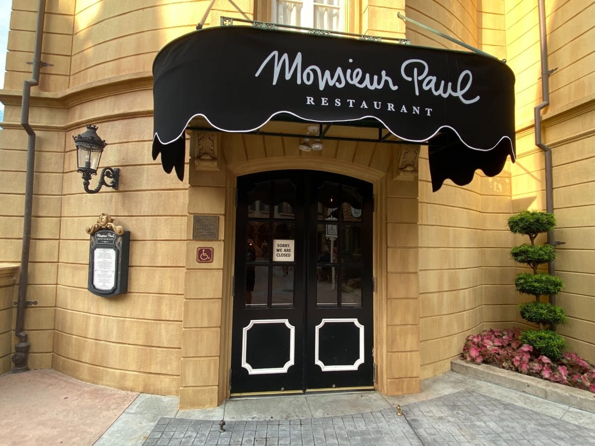 Entrance of Monsieur Paul Restaurant, one of the premier EPCOT Restaurants, features a black awning, double doors, and menu outside.