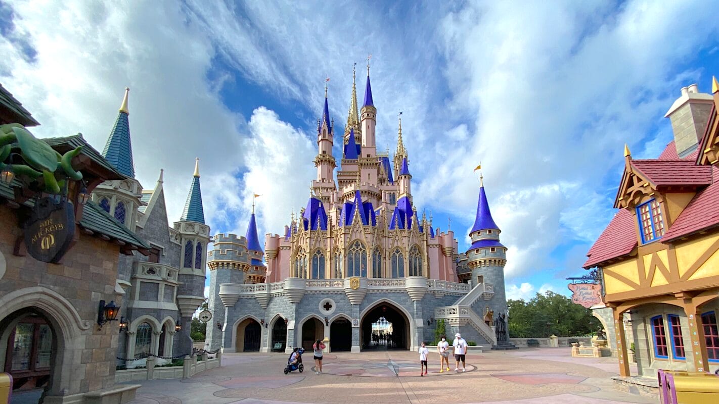 Cinderella Castle at Disney World with blue sky, fluffy clouds, and a few visitors walking nearby. Cinderella Castle at Disney World from Fantasyland with blue sky, fluffy clouds, and a few visitors walking nearby.