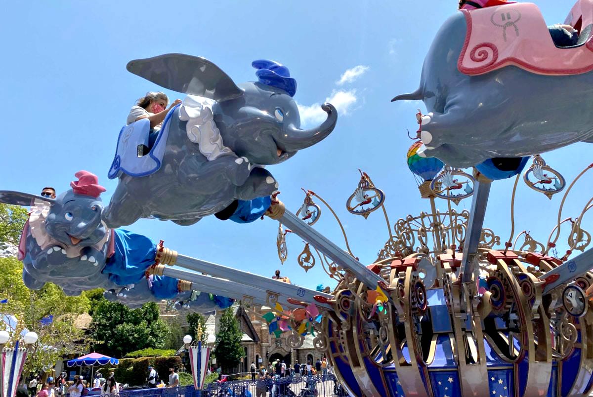 Children ride flying Dumbo elephant cars on a spinning amusement park ride under a sunny blue sky. Ride flying Dumbo the Elephant in Fantasyland