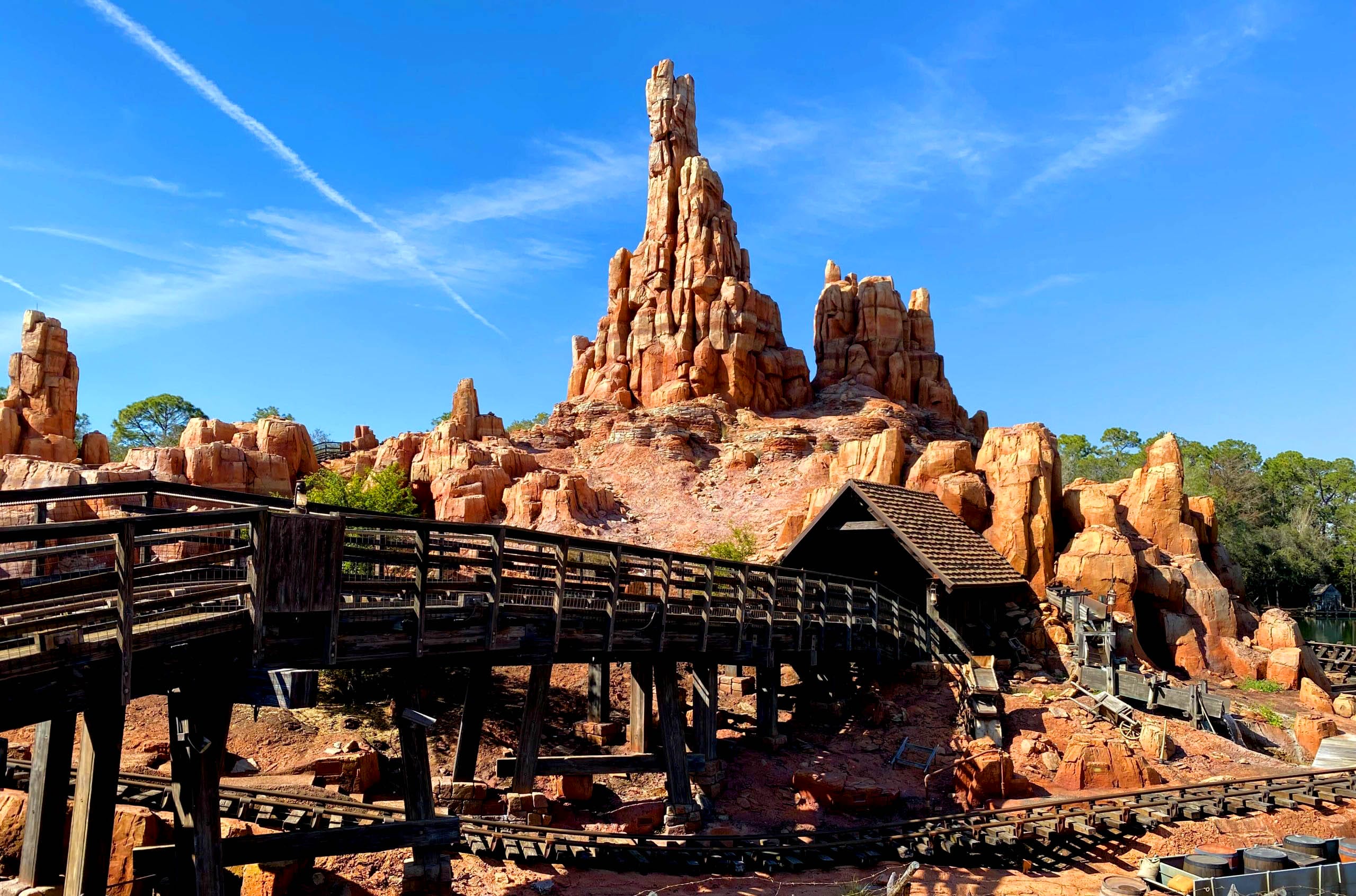 Big Thunder Mountain Railroad runs through red rock formations in Frontierland under a clear blue sky.