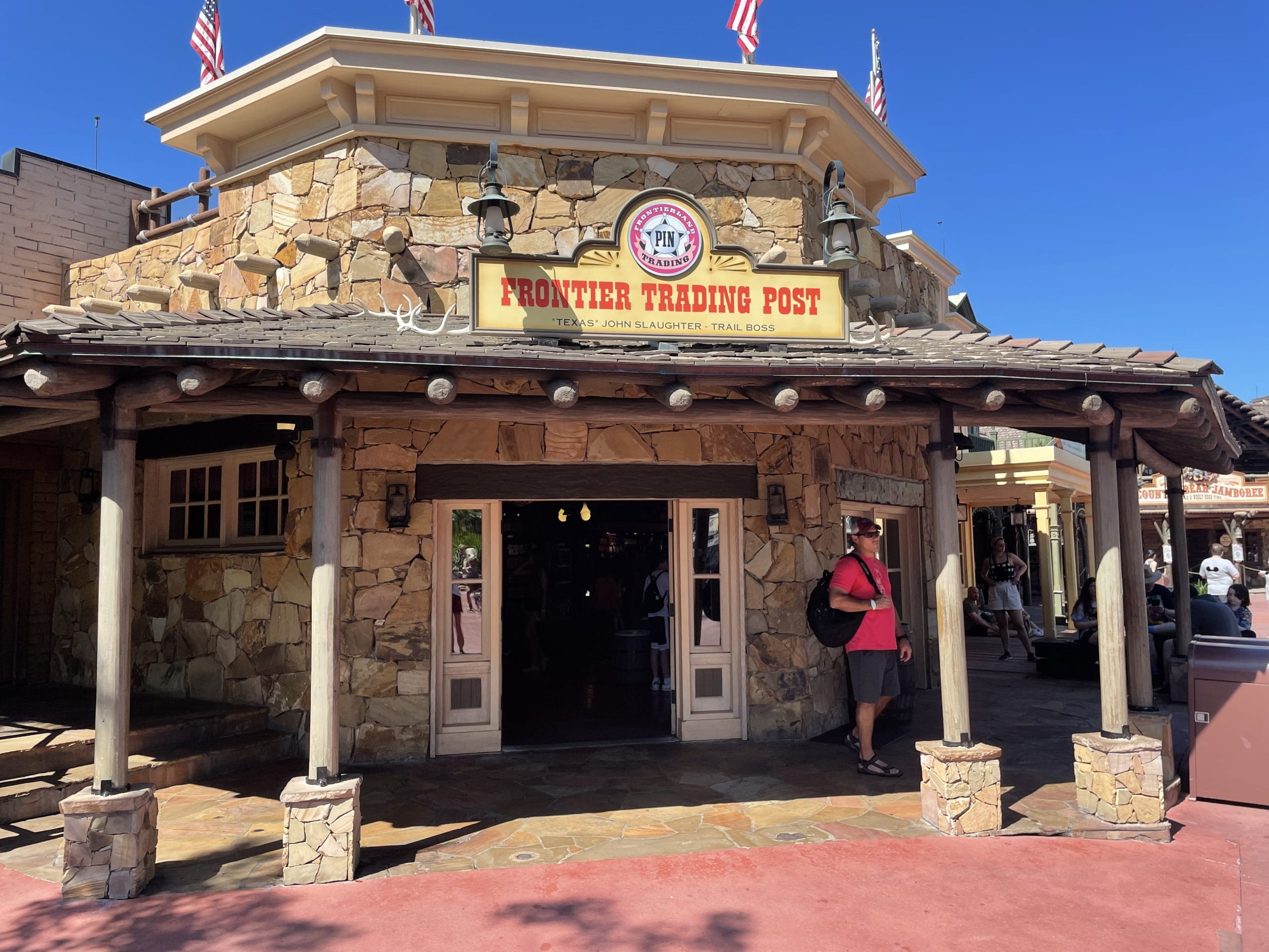 Frontier Trading Post in Frontierland. A stone building with a wooden porch and sign, under a clear blue sky.