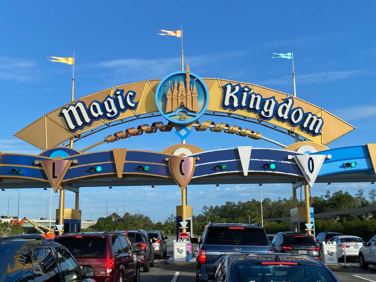 Cars wait in line at the Magic Kingdom Toll Plaza with a blue sky and trees in the background.