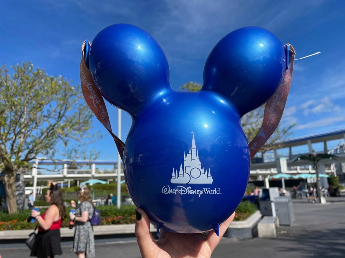 A hand holds a blue Balloon shaped Disney Popcorn Bucket with a "Walt Disney World 50" logo