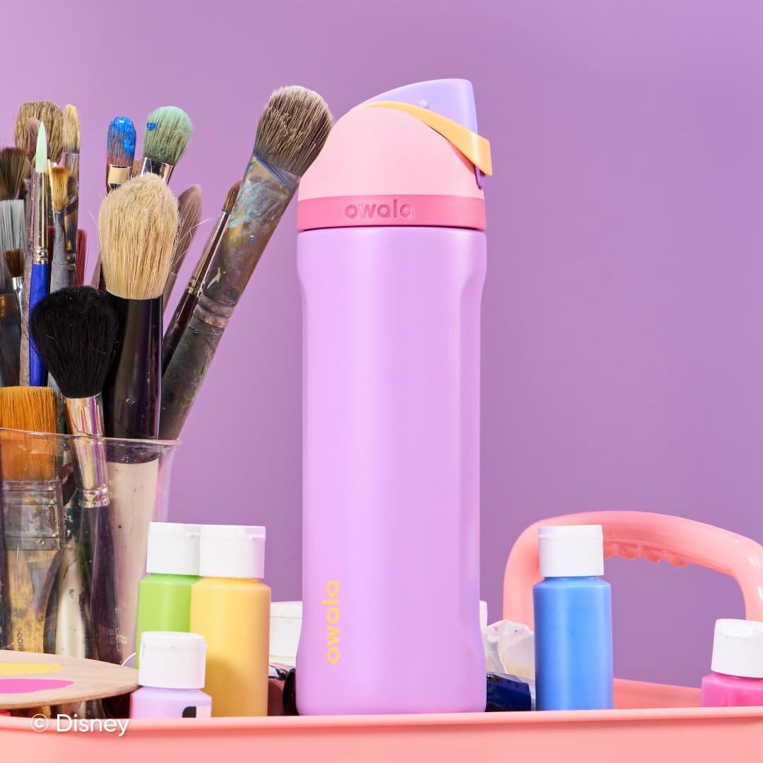 A purple and pink Owala water bottle sits on a tray with paintbrushes and colorful paints, against a purple background.