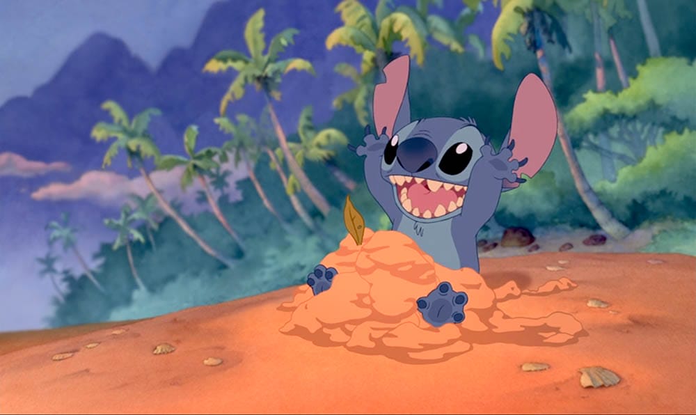 Stitch, a blue alien, plays happily on a sandy beach—perfect for your Stitch Wallpaper or Free Downloads.