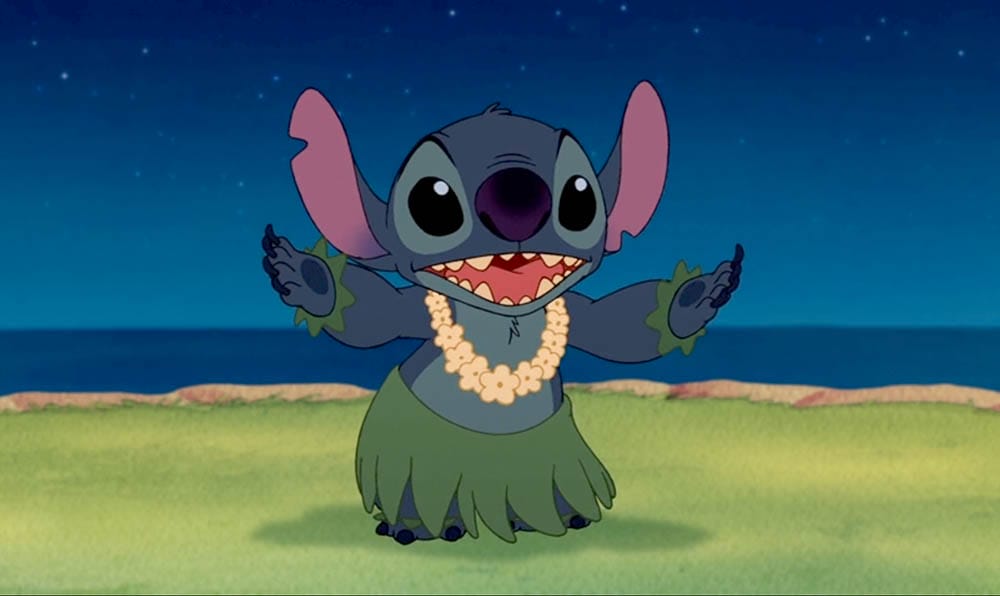 Stitch from Lilo & Stitch in a grass skirt and lei, smiling with arms raised—perfect Stitch wallpaper for free downloads!