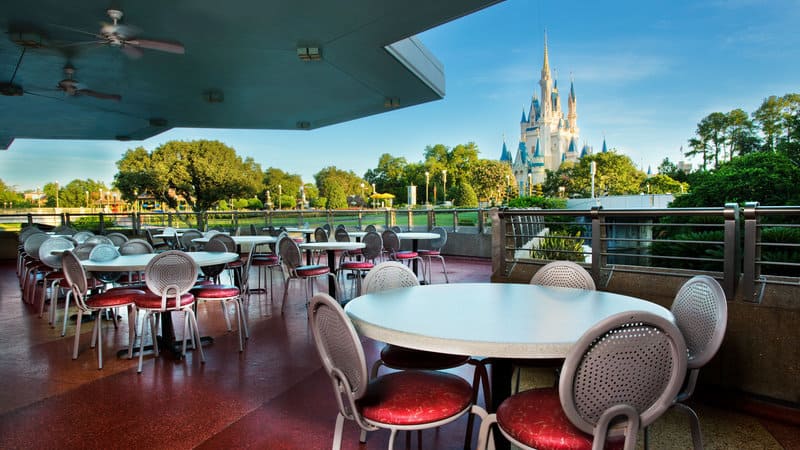 Outdoor dining area with empty tables and chairs, overlooking Tomorrowland castle and lush greenery in the distance. Outdoor dining area with empty tables and chairs, inTomorrowland overlooking cinderella castle and lush greenery in the distance.
