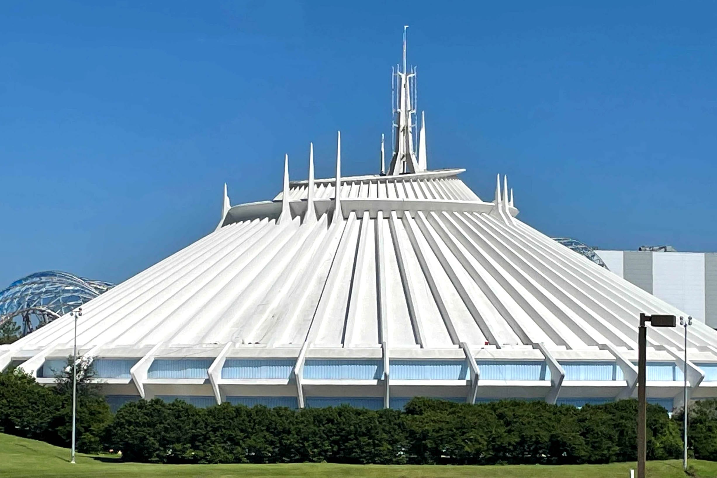 A futuristic white Tomorrowland building with spires, resembling a space-themed structure, against a clear blue sky. Space mountain in Tomorrowland building with spires, resembling a space-themed structure, against a clear blue sky.