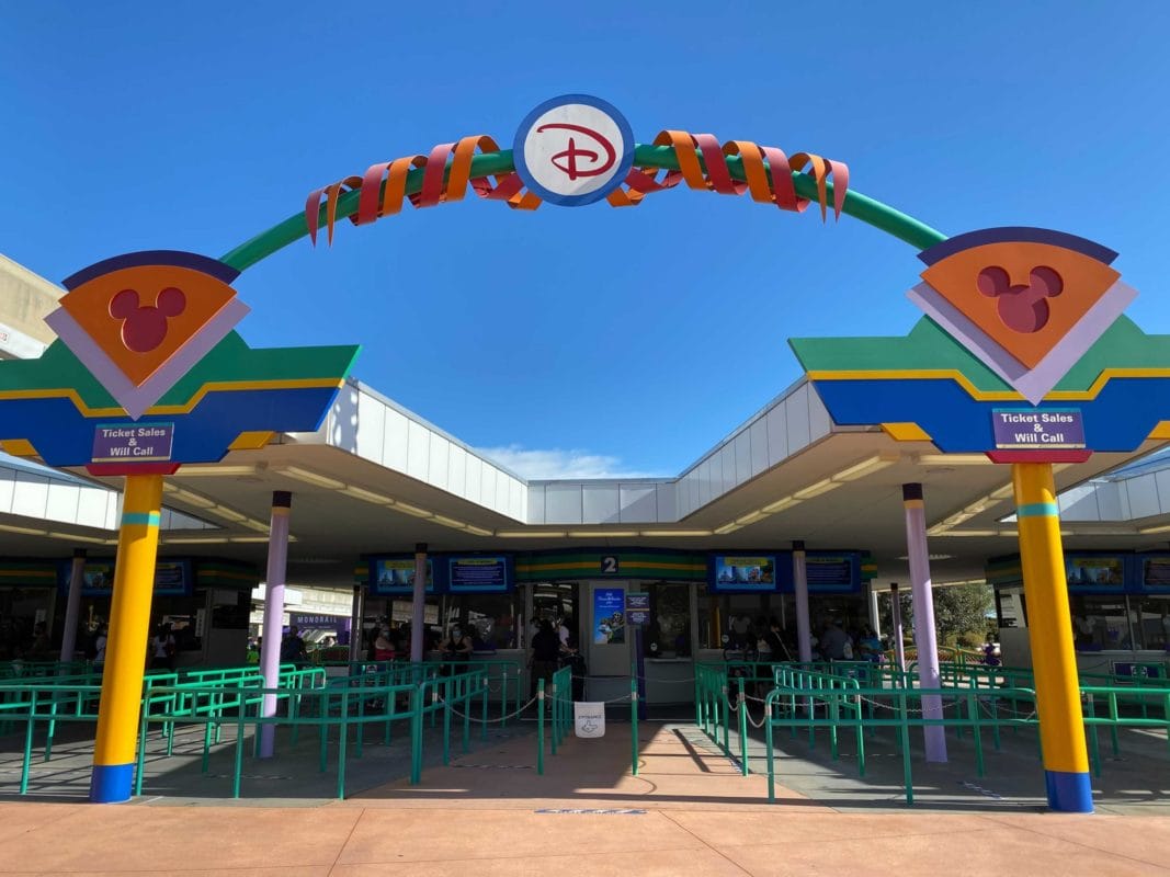 Entrance gate to Disney’s Magic Kingdom Ticket Center with colorful signs, logo, and green queue barriers under a blue sky after going through the magic kingdom toll plaza.