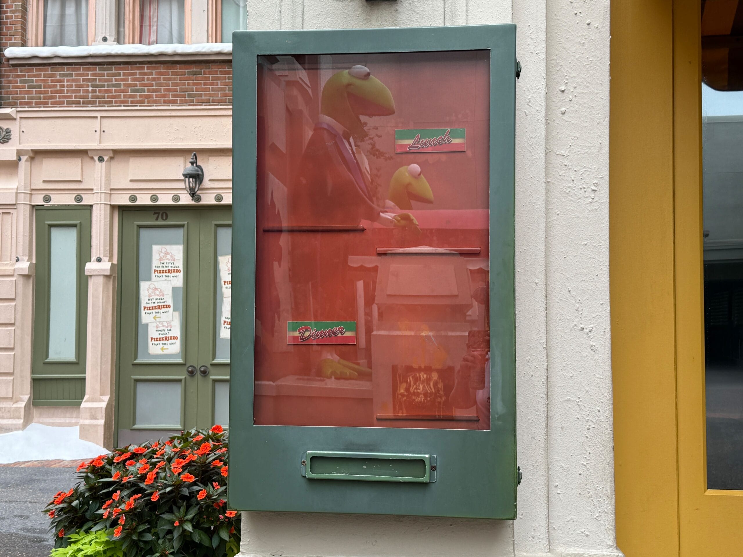 A faded poster of Kermit the Frog in a green frame decorates a wall near flowers at Disney's Hollywood Studios.