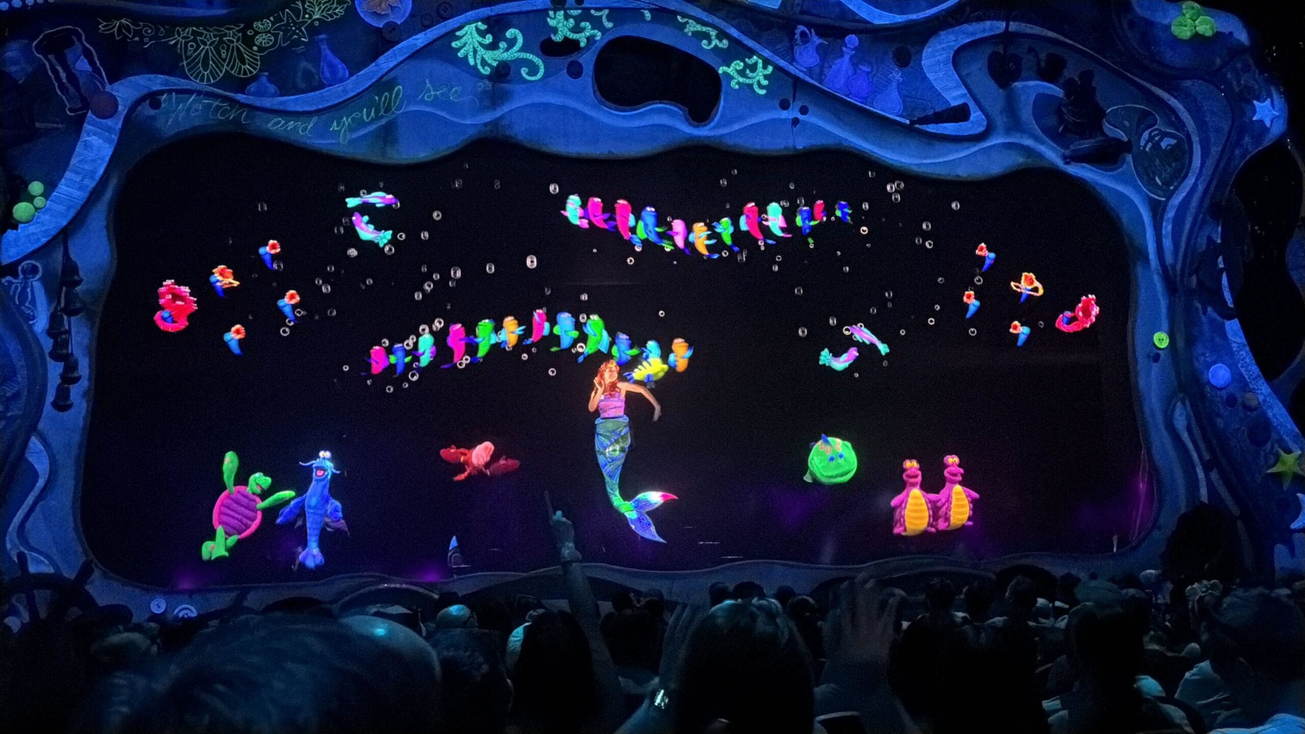 A stage show, Little Mermaid: A Musical Adventure, features glowing sea creatures and a mermaid under blacklight.