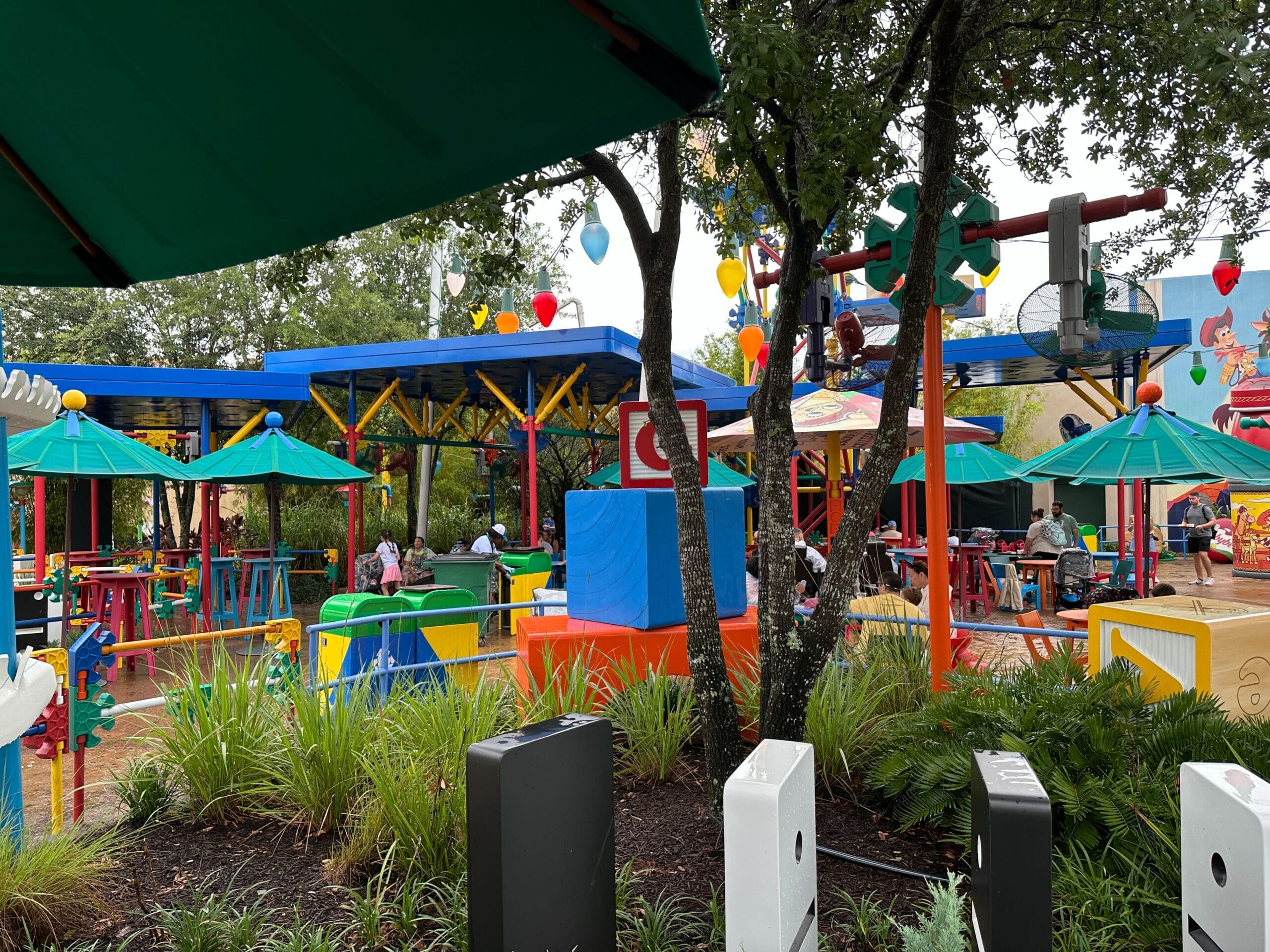 Colorful outdoor seating area with green umbrellas, tables, plants, and playful decorations resembling toys.