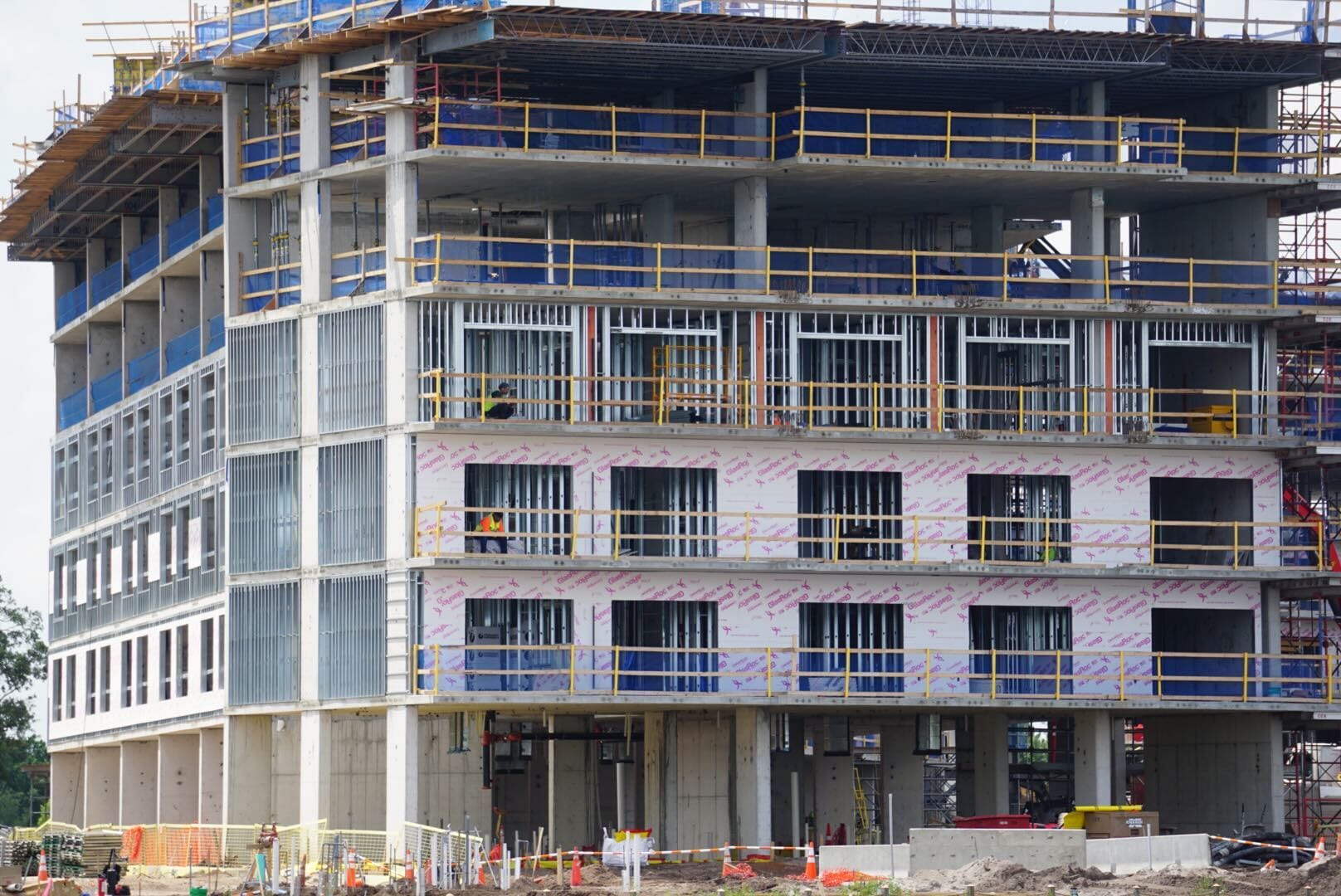 A multi-story building under construction, with exposed steel beams, scaffolding, and unfinished exterior walls.