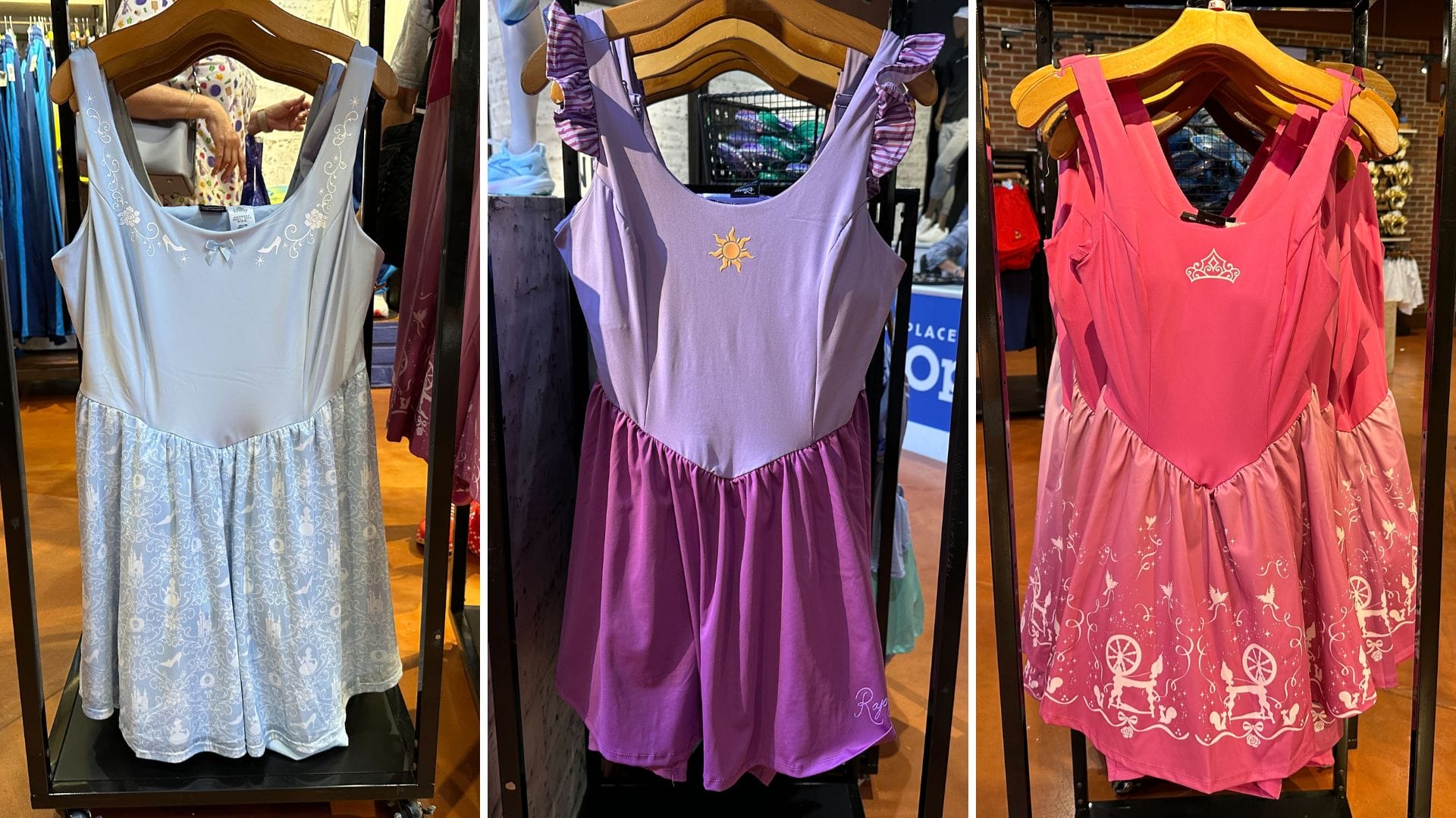 Three Disney Princess dresses for kids, elegantly displayed on wooden hangers in a charming clothing store.