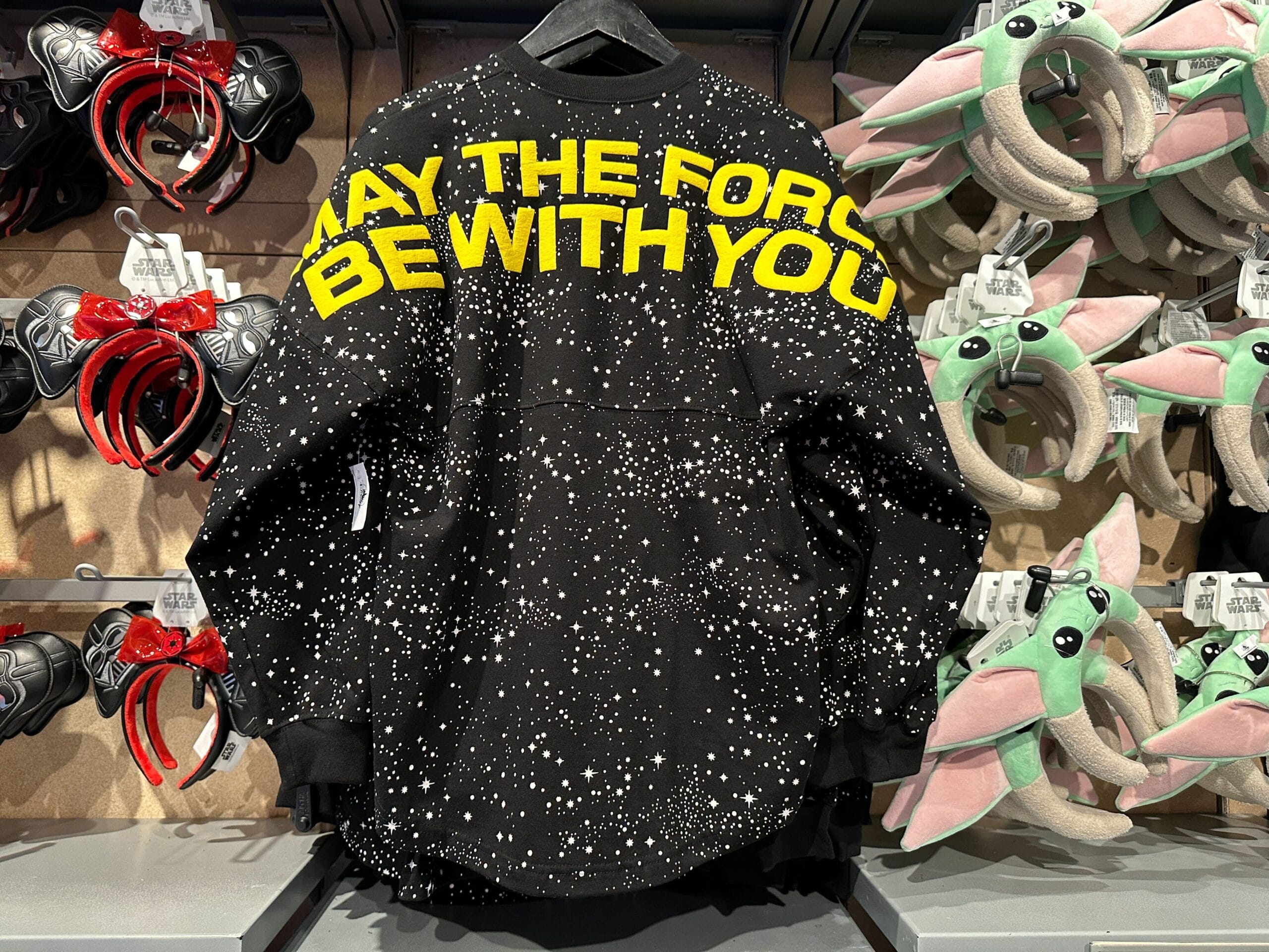 Black sweatshirt with yellow "May the Force Be With You" text and stars, perfect for celebrating May the 4th at Walt Disney World.