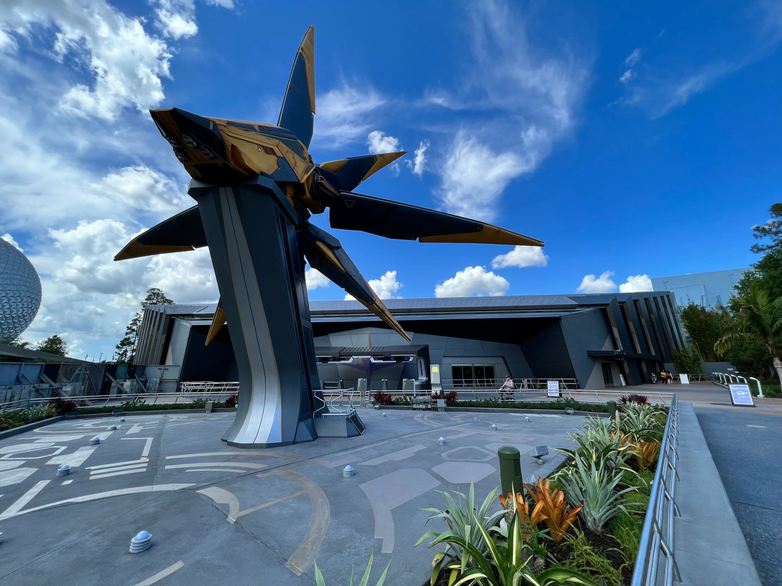 A large Guardians of the Galaxy spaceship sculpture stands outside a modern building under a bright blue sky with clouds - Cosmic Rewind Ride Songs
