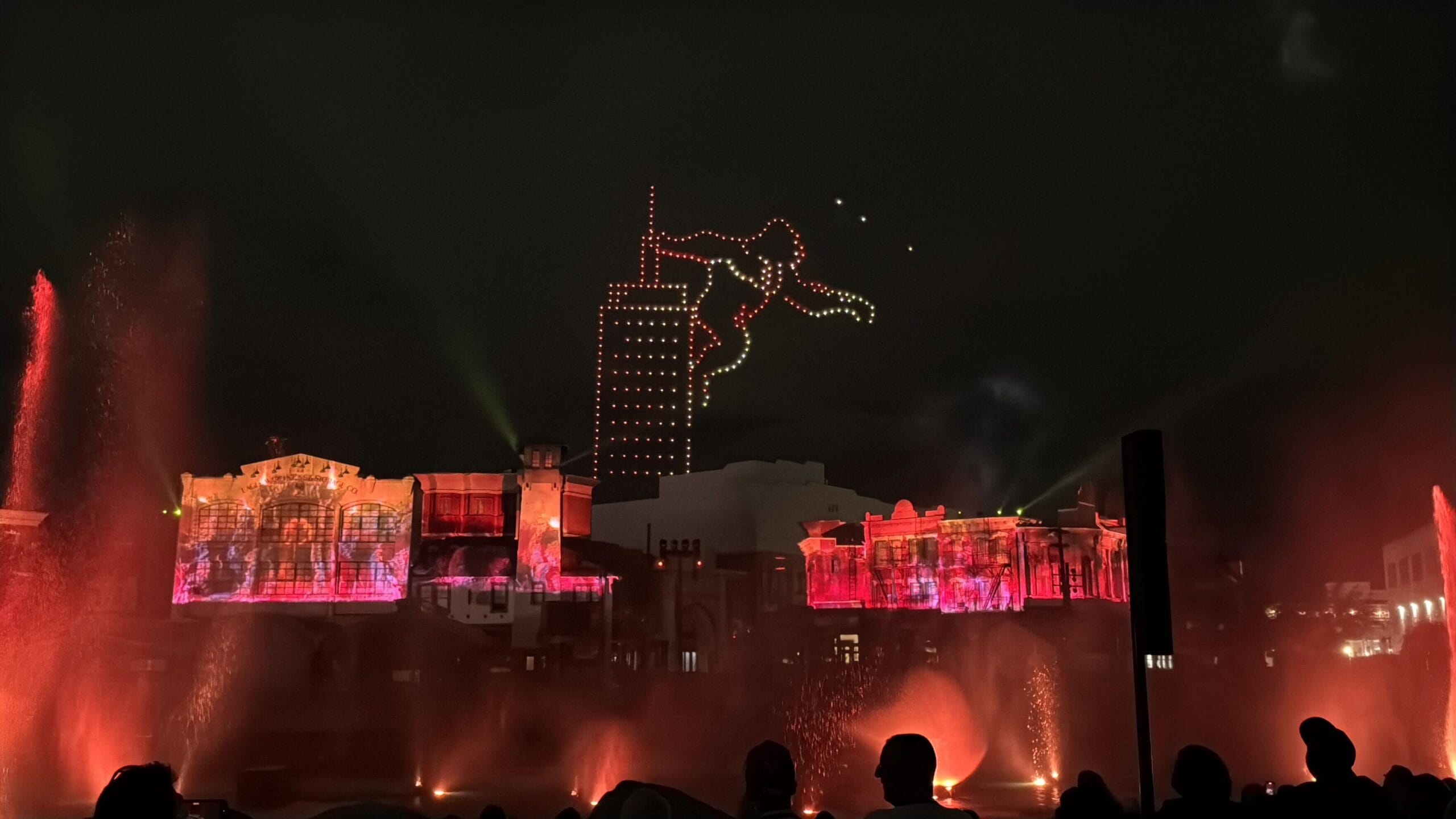 A nighttime water and light show at Universal Studios Florida with drones forming a superhero over illuminated buildings.