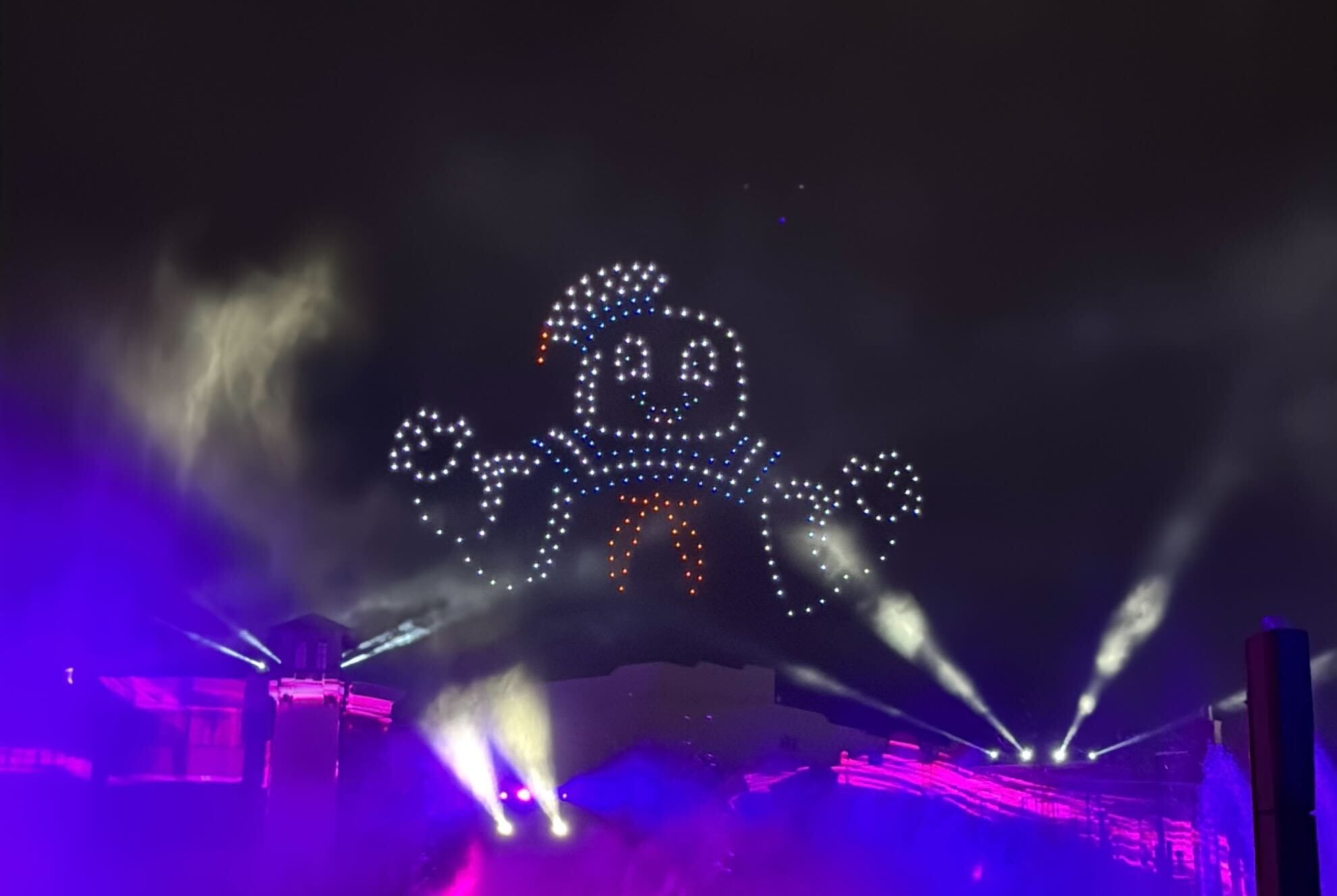 A smiling marshmallow made of lights, part of Universal Studios Florida’s CineSational Nighttime Spectacular, floats above drones.