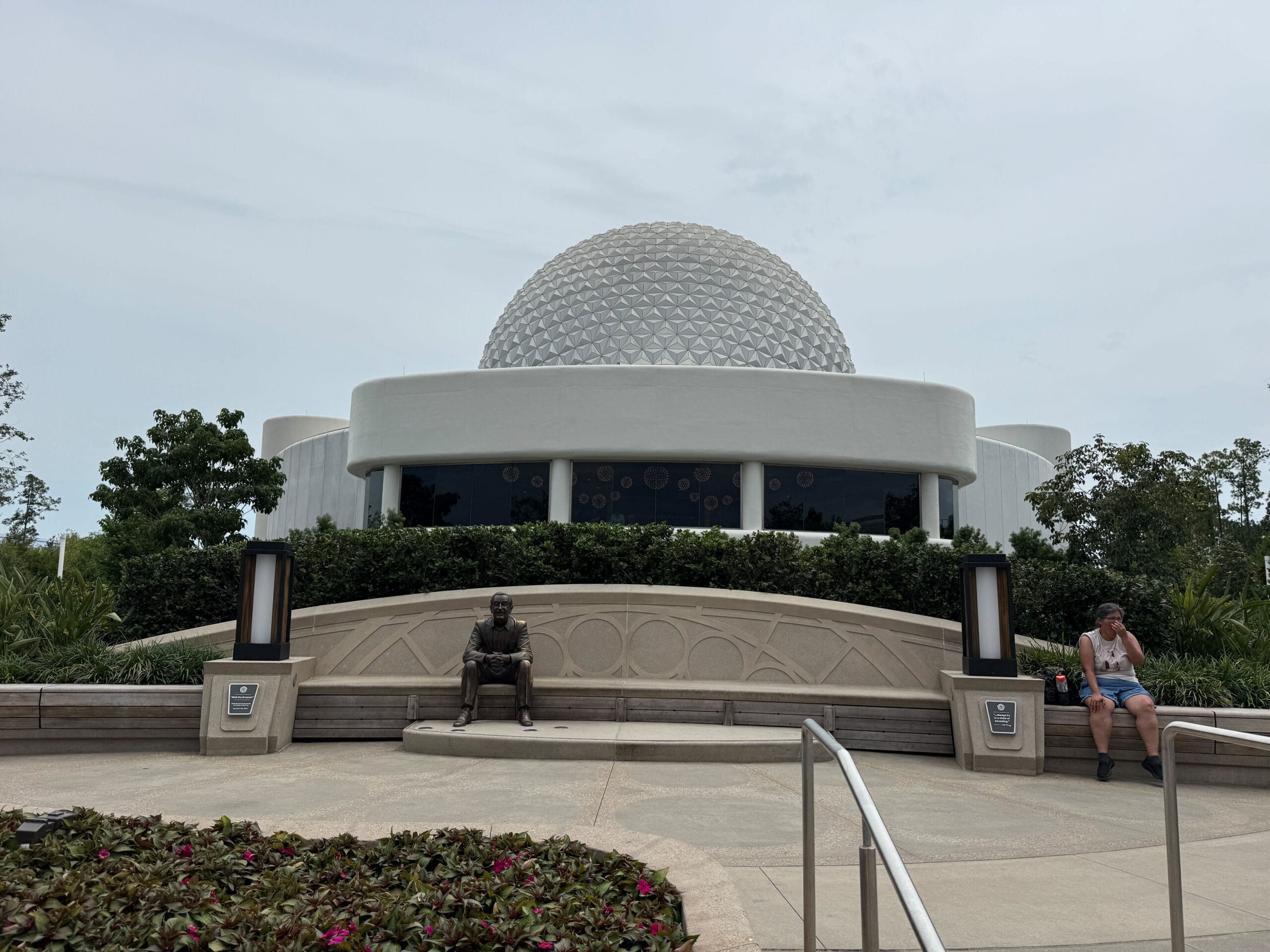 White geodesic dome building near Dreamers Point, with a bronze seated statue and two people relaxing on benches.