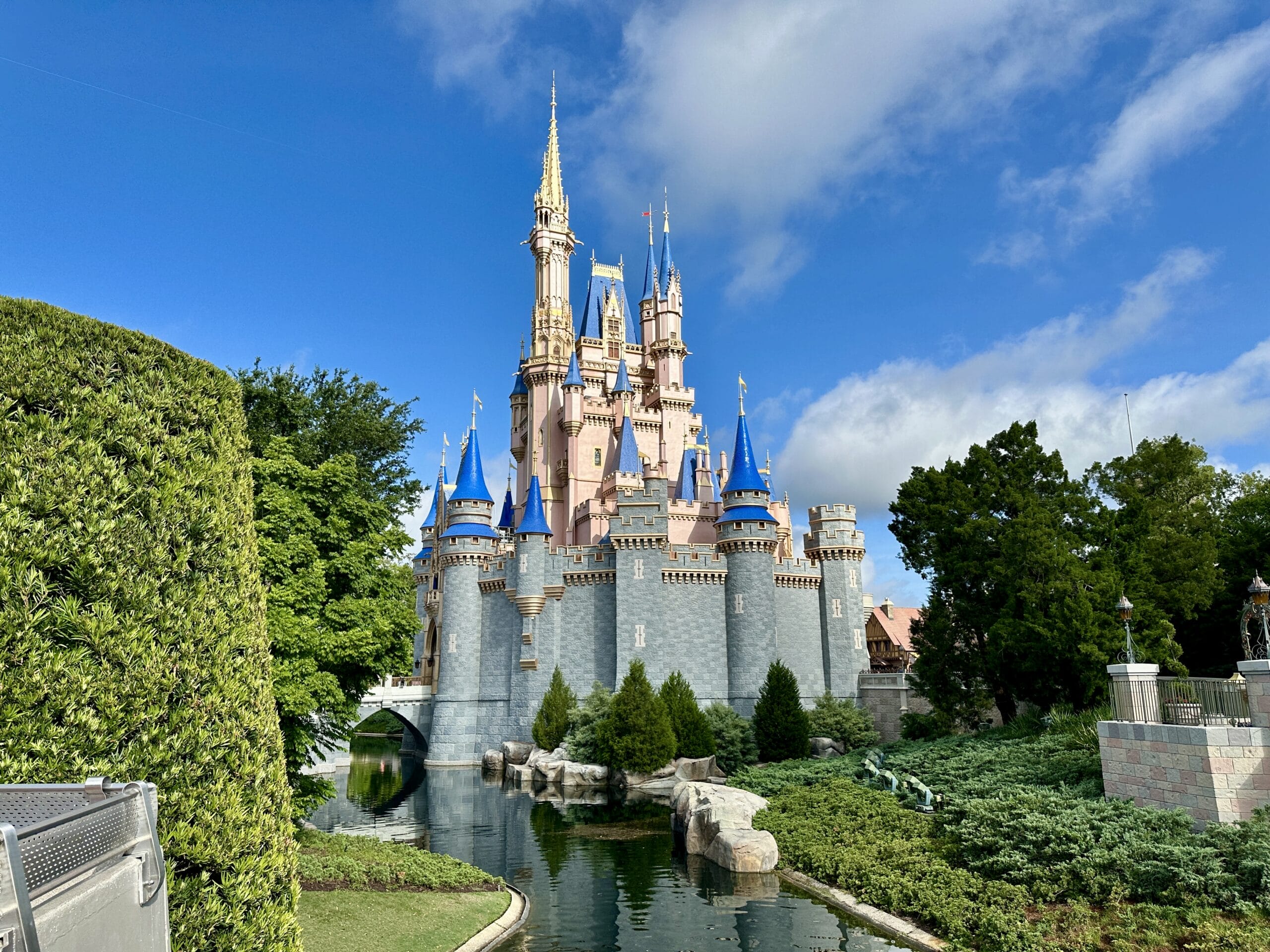Cinderella Castle at Magic Kingdom, surrounded by trees, a moat, and bright blue sky with fluffy clouds.