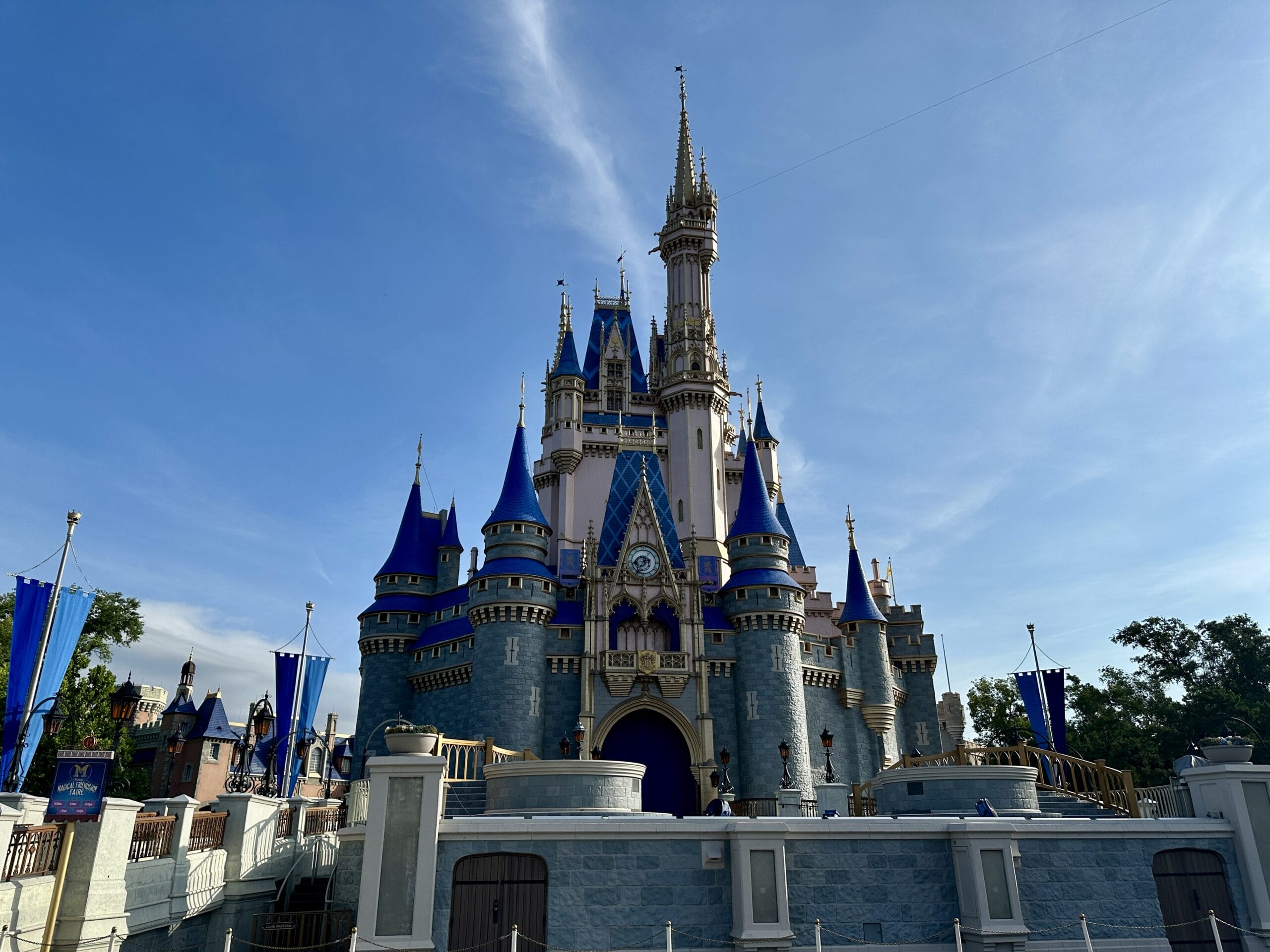 Cinderella Castle at Magic Kingdom, with blue spires and gold accents, shines under a clear blue sky.