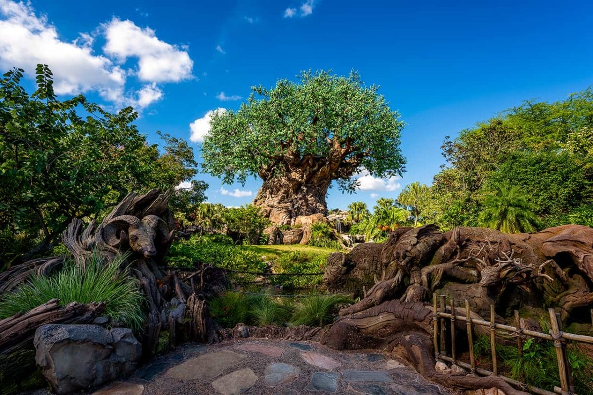 The tree of life at animal kingdom with carved animal figures recalls Disney World amid lush greenery and a bright blue sky.
