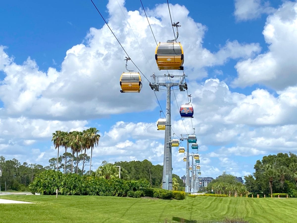 Yellow gondola skyliner cars soar above green trees under a blue sky