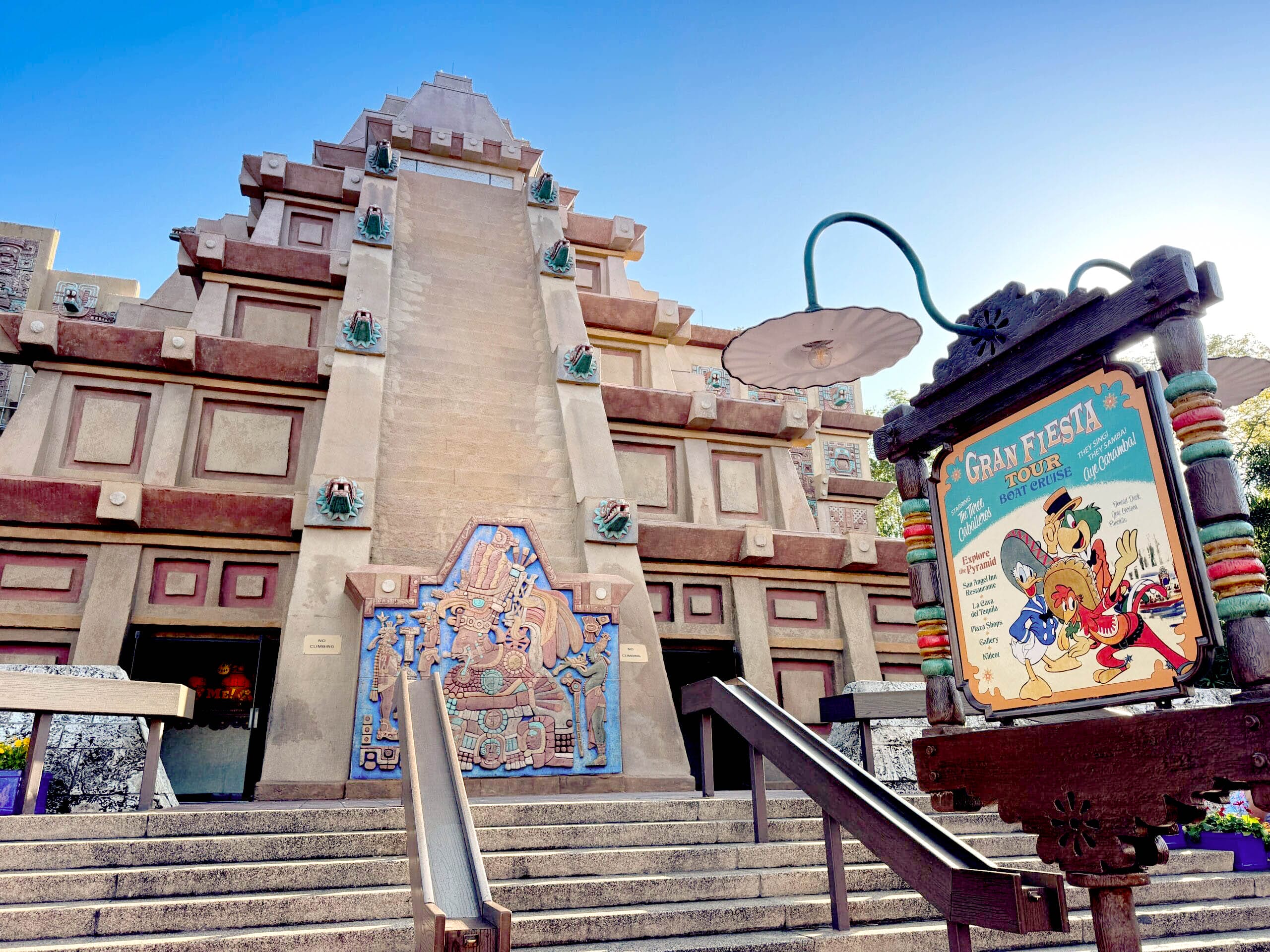 A pyramid-shaped building with Mayan-style art and a colorful "Gran Fiesta Tour" sign featuring Disney characters - one of the EPCOT rides
