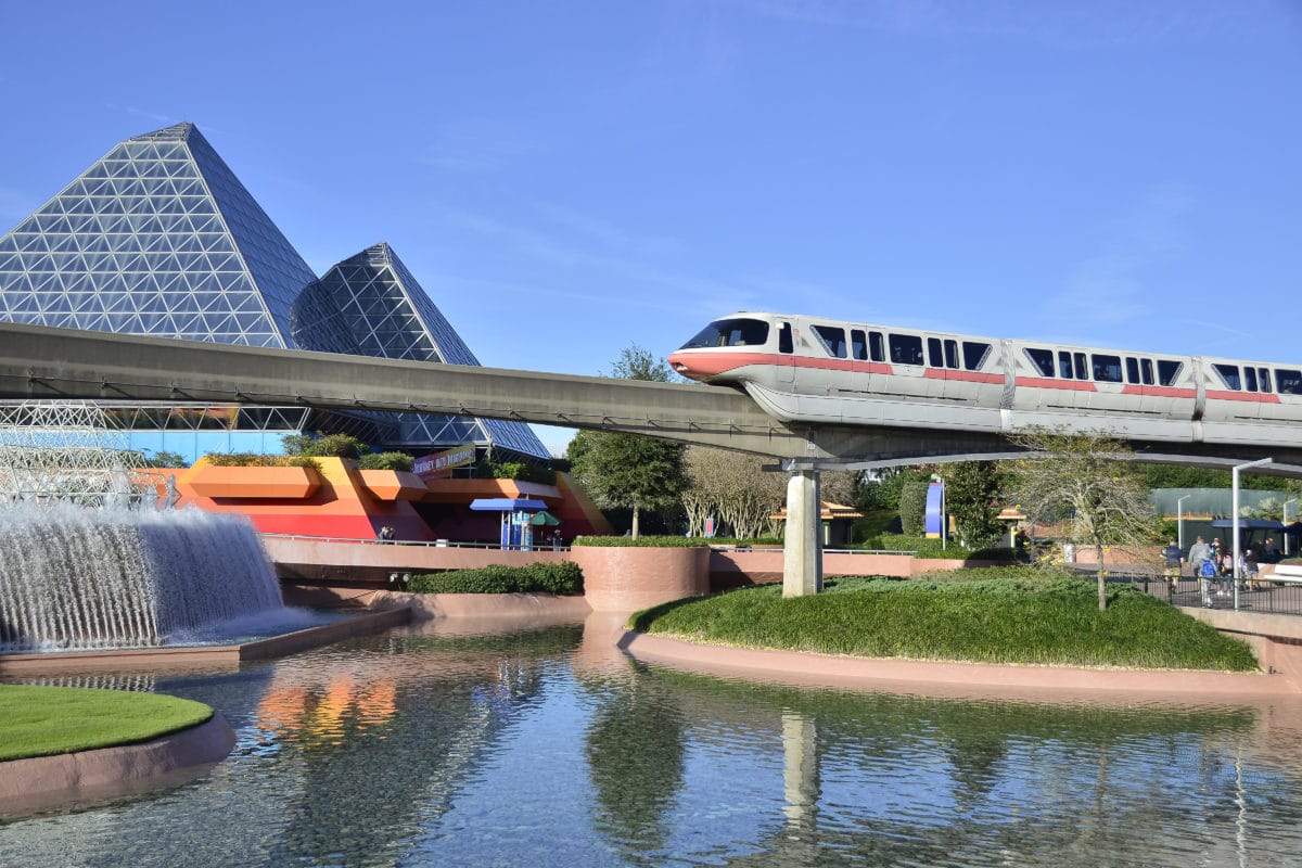 A monorail glides over water near glass pyramids, perfect for Disney World park hopping on a sunny day.
